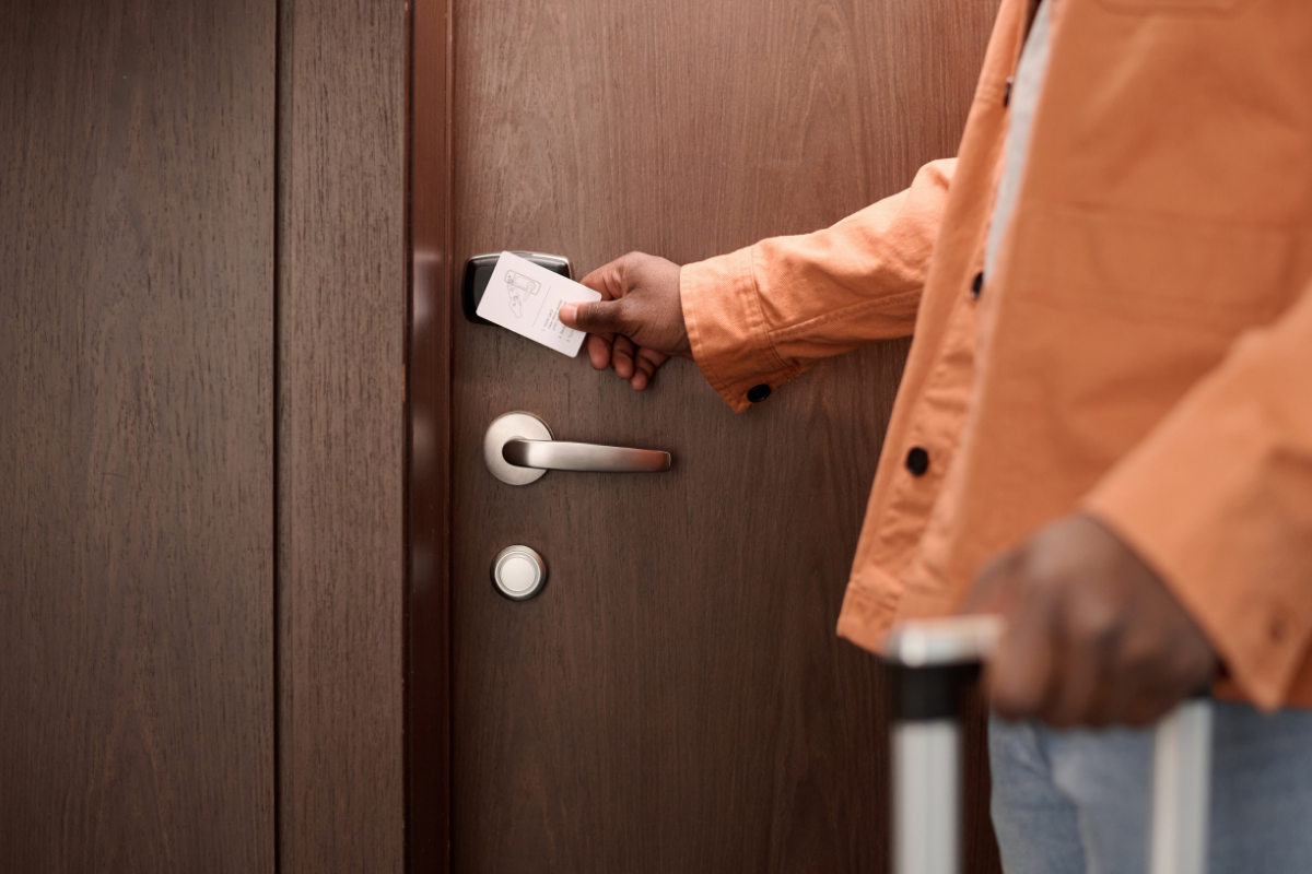 A person in an orange jacket inserting a key card into a door lock to unlock the door.