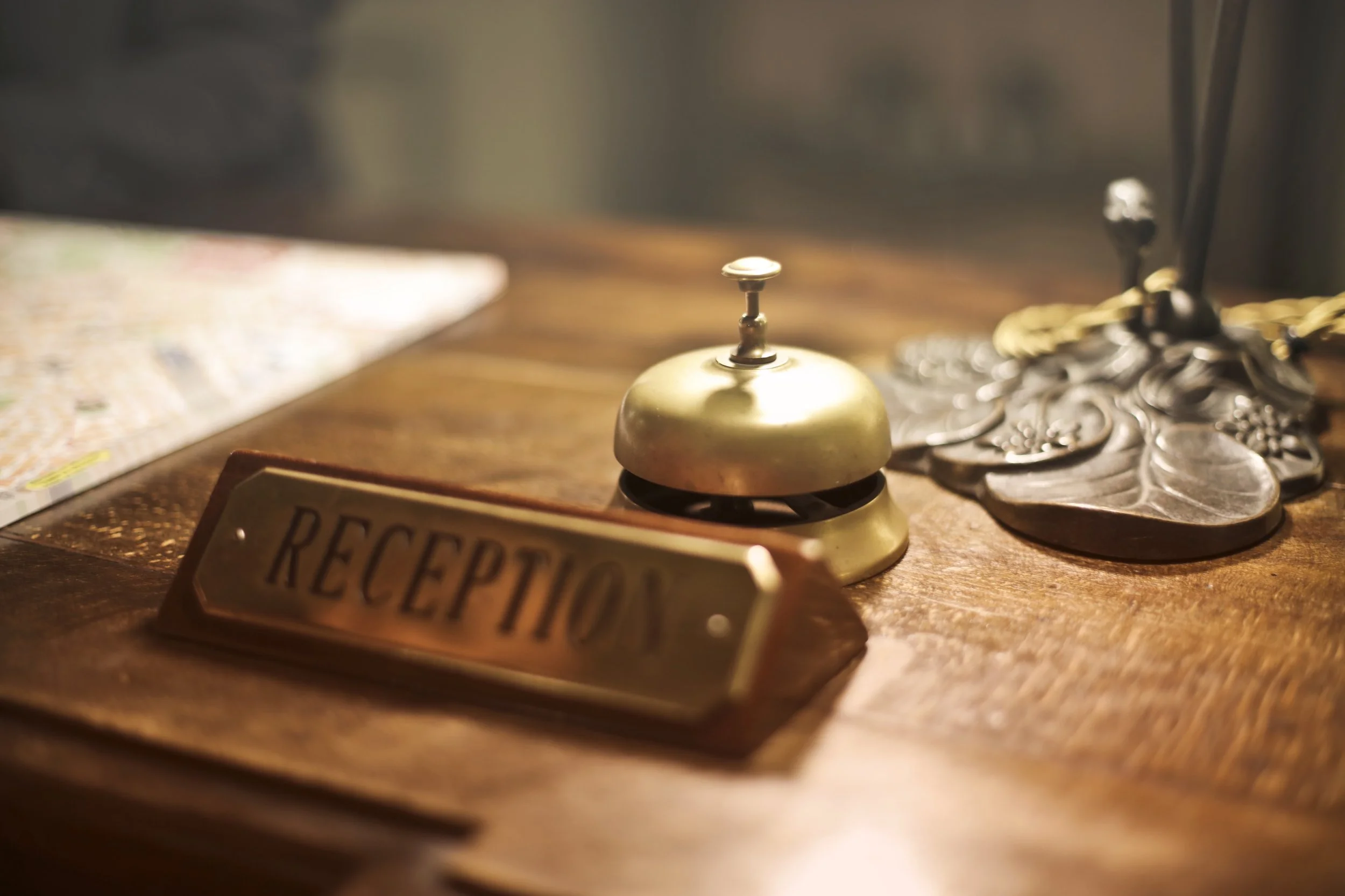 A small brass bell on a wooden surface, with a collection of silver coins and a 'Reception' sign nearby.