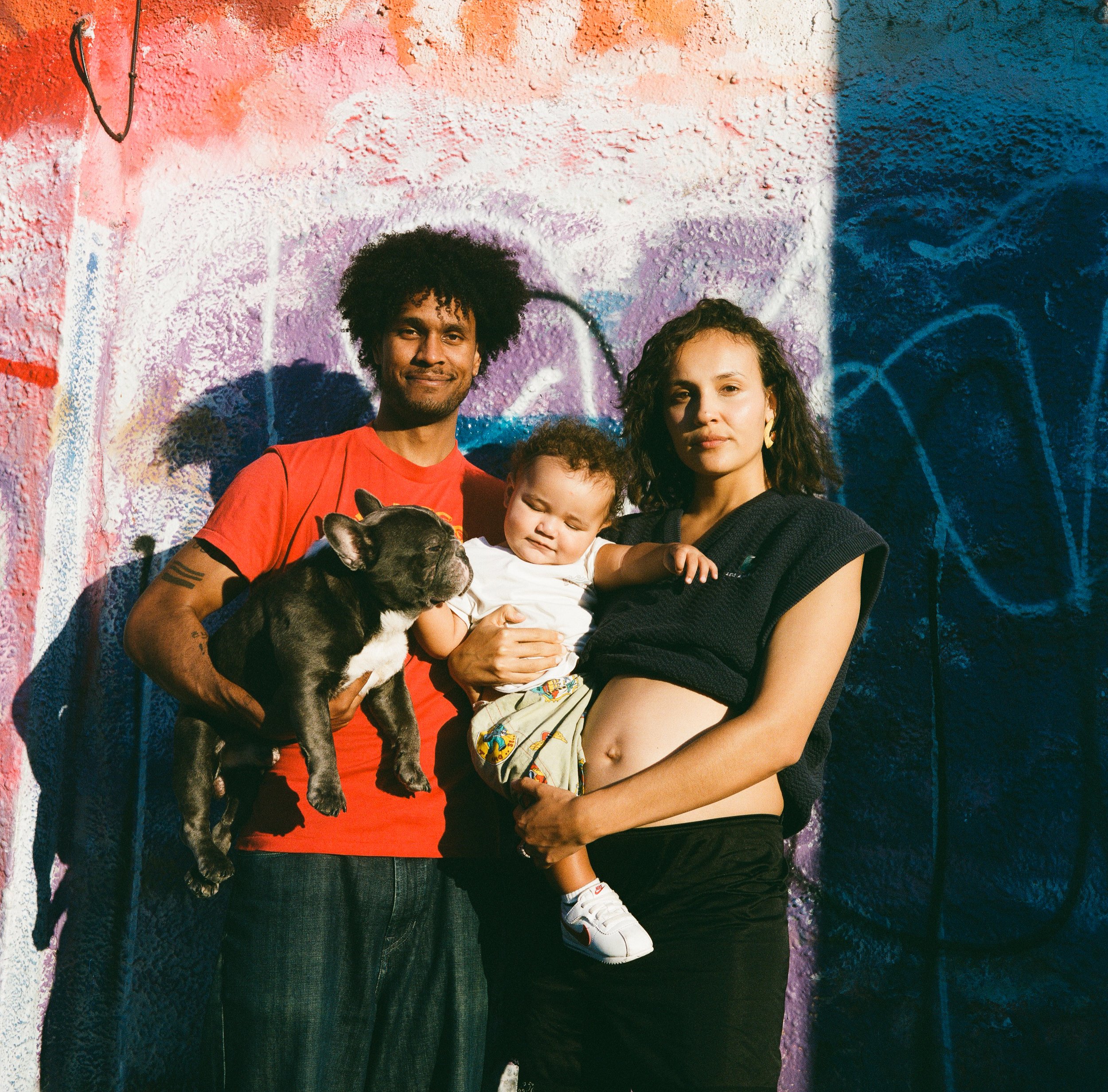 A group of diverse young people and a dog are standing in front of a colorful, graffiti-covered wall.