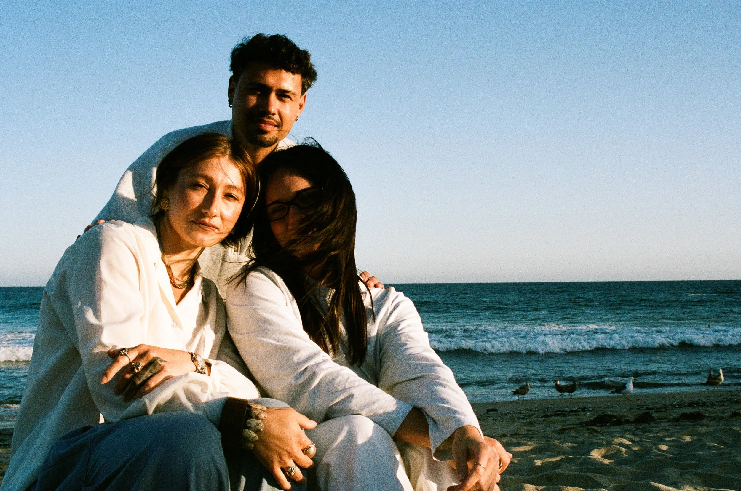 Three people sitting by the beach with seagulls and ocean in the background.