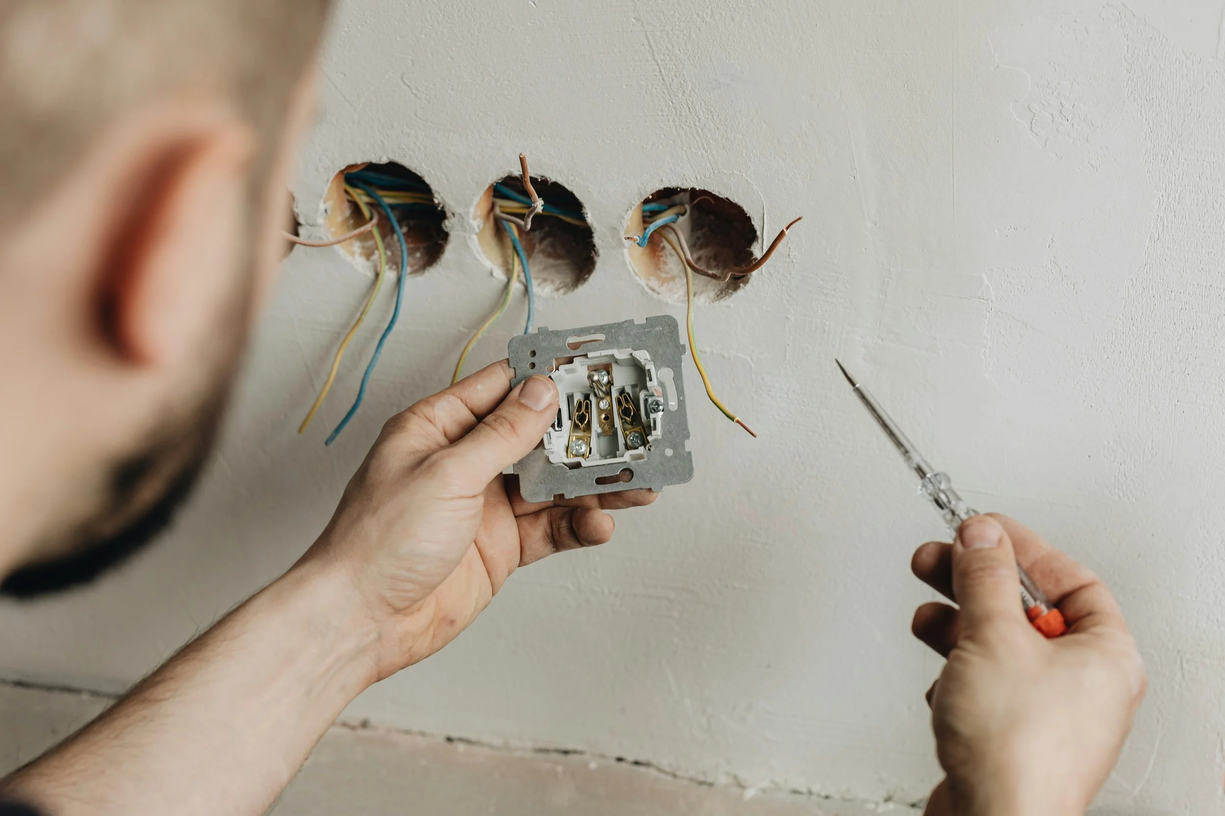 Person installing or repairing electrical wiring in a wall with multiple holes and a metal electrical box.