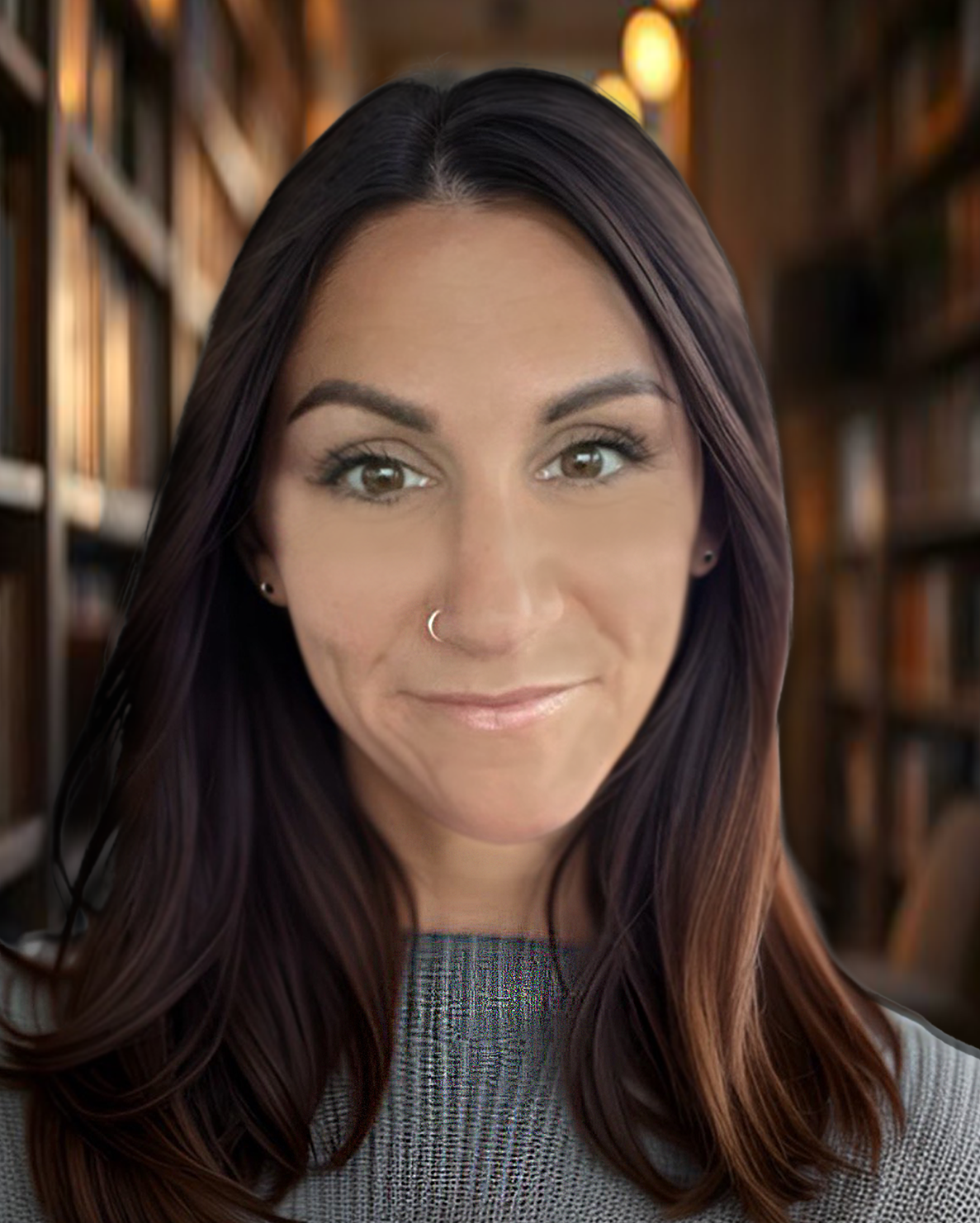 A young woman with dark hair, brown eyes, and a nose piercing in a library setting, smiling softly.