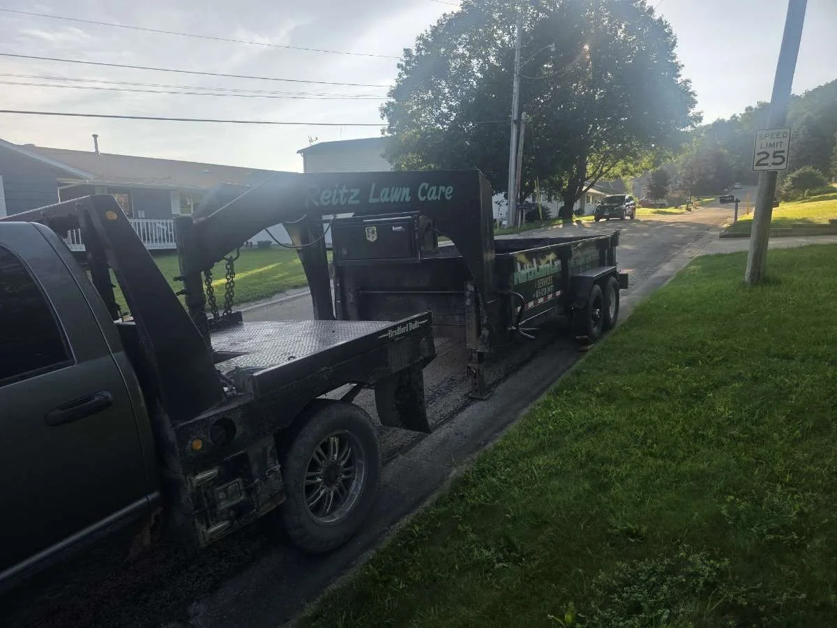 A tow truck parked on the side of a residential street with houses, trees, and a speed limit sign that reads 25 mph in the background.