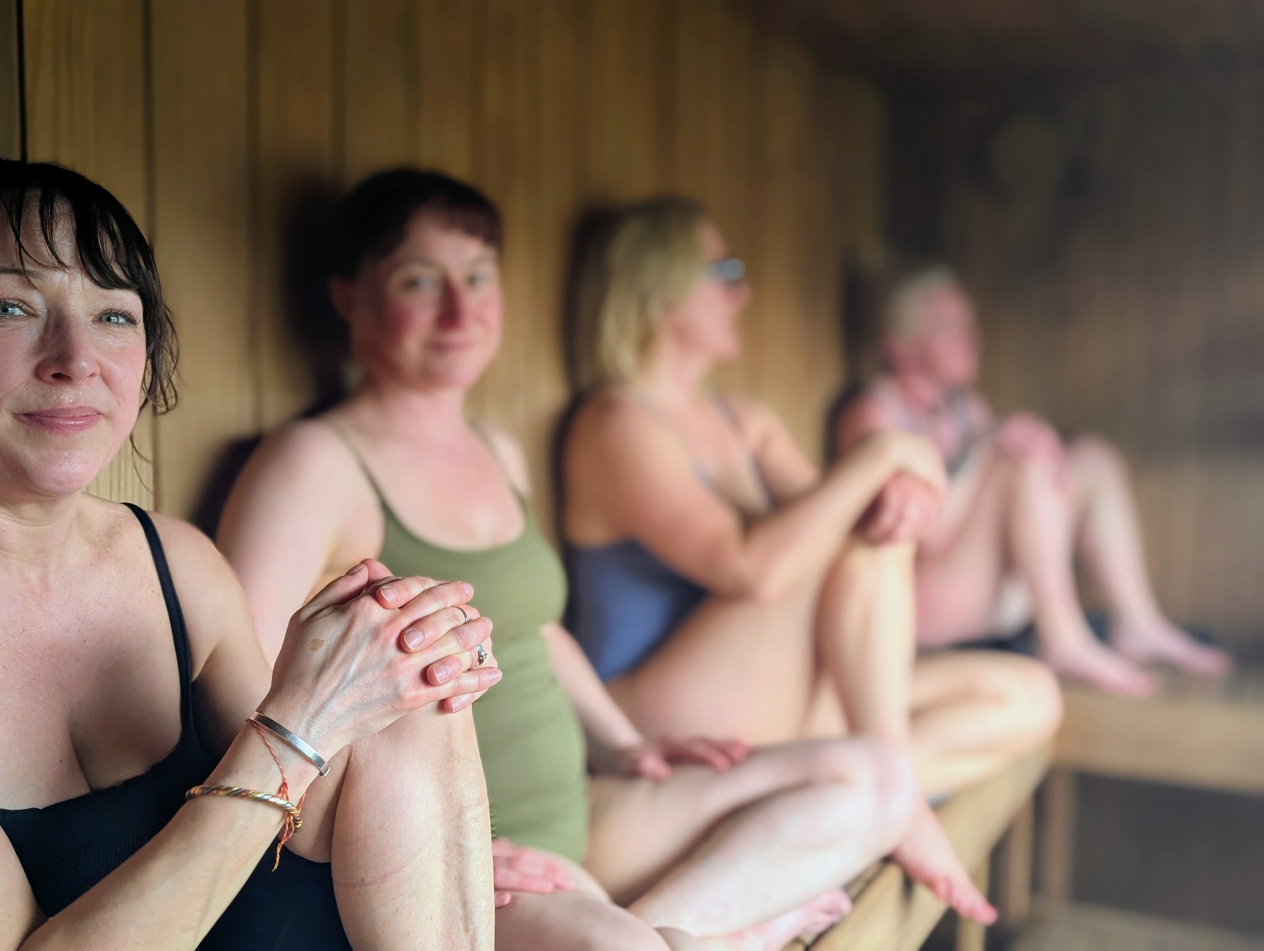 A line of women seated with their hands clasped, participating in relaxing outdoor sauna session