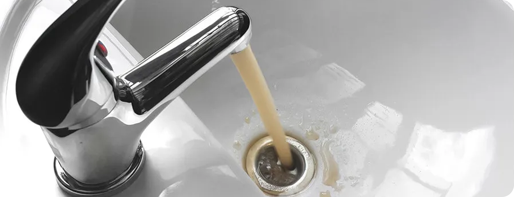 A kitchen sink with hot water running from a modern chrome faucet, filling the drain with brown liquid.