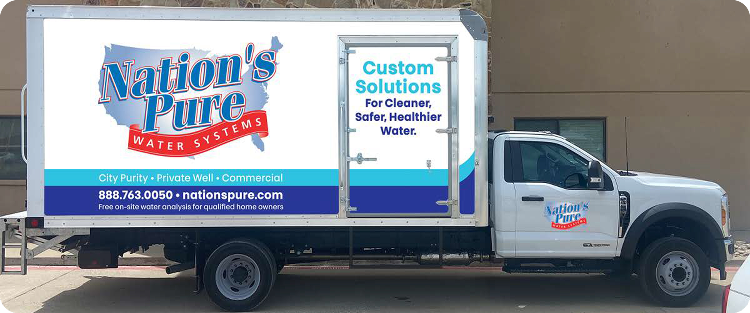 A white truck with signage for Nation's Pure Water Systems parked outside a building. The sign includes a logo with a map outline of the United States, and text promoting custom water solutions, city purity, private wells, and commercial services.