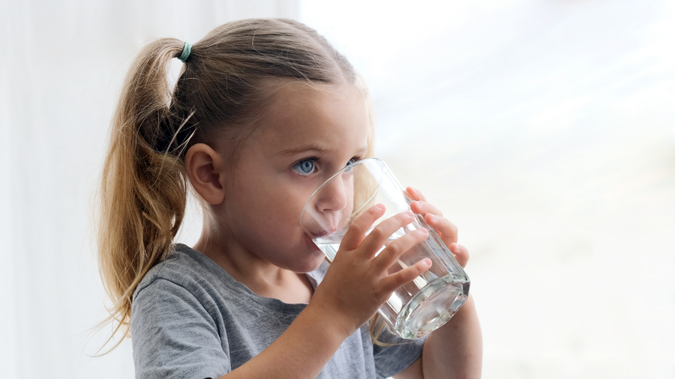 Young girl with blonde hair in a ponytail drinking water from a clear glass