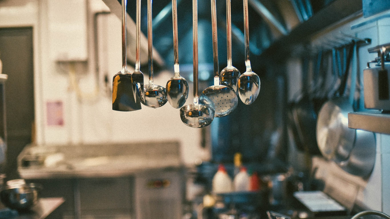Clean, spot-free stainless steel utensils hanging above a commercial kitchen food prep station.
