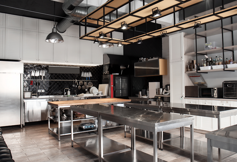A professional commercial kitchen with stainless steel counters, hanging pots and pans, and shelves with kitchen supplies.