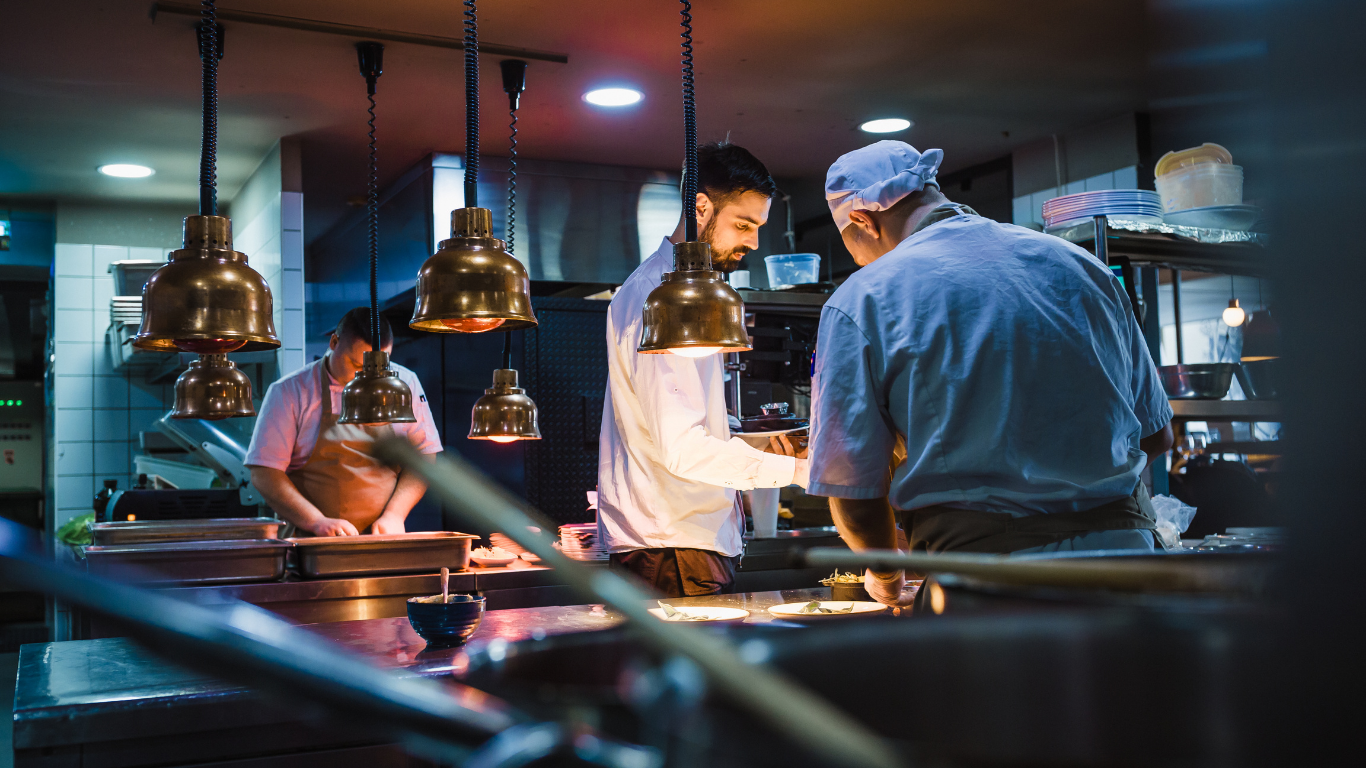 Chefs plating dishes under heat lamps in a restaurant kitchen supported by a commercial water treatment company near me.
