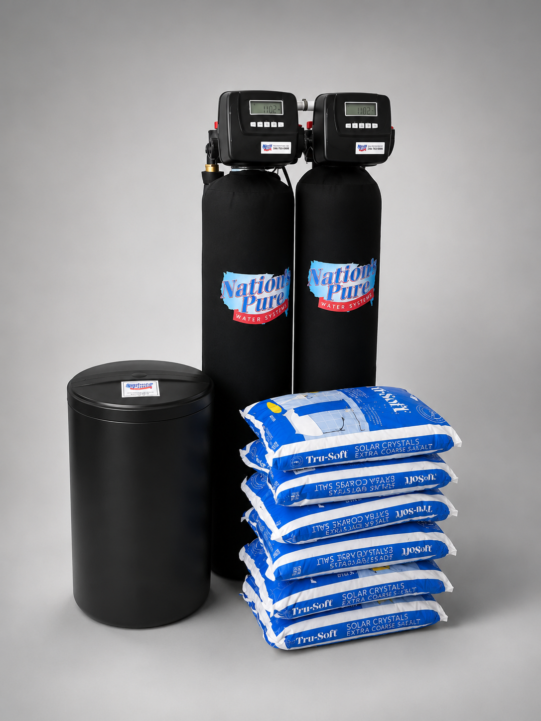 Two black water softener tanks with digital displays, a black brine tank, and bags of solar crystals salt for water softening on a gray background.
