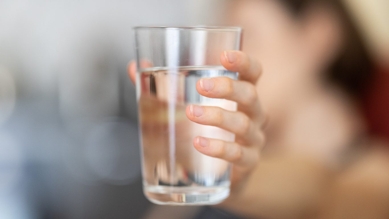 Person holding a clear glass of tap water to inspect for smells and clarity from a private well.