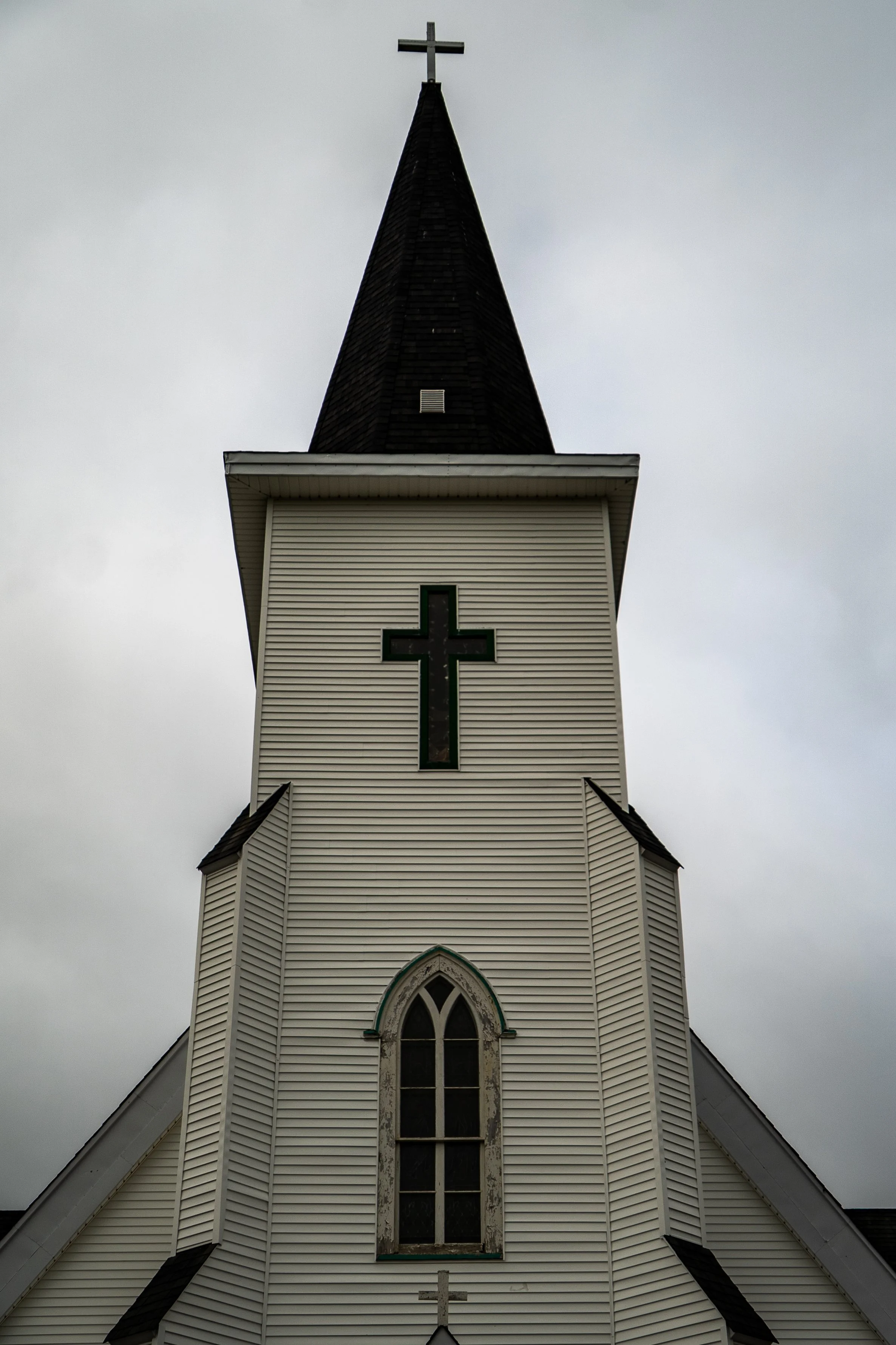 A white church building with a tall steeple topped with a cross, overcast sky in background.