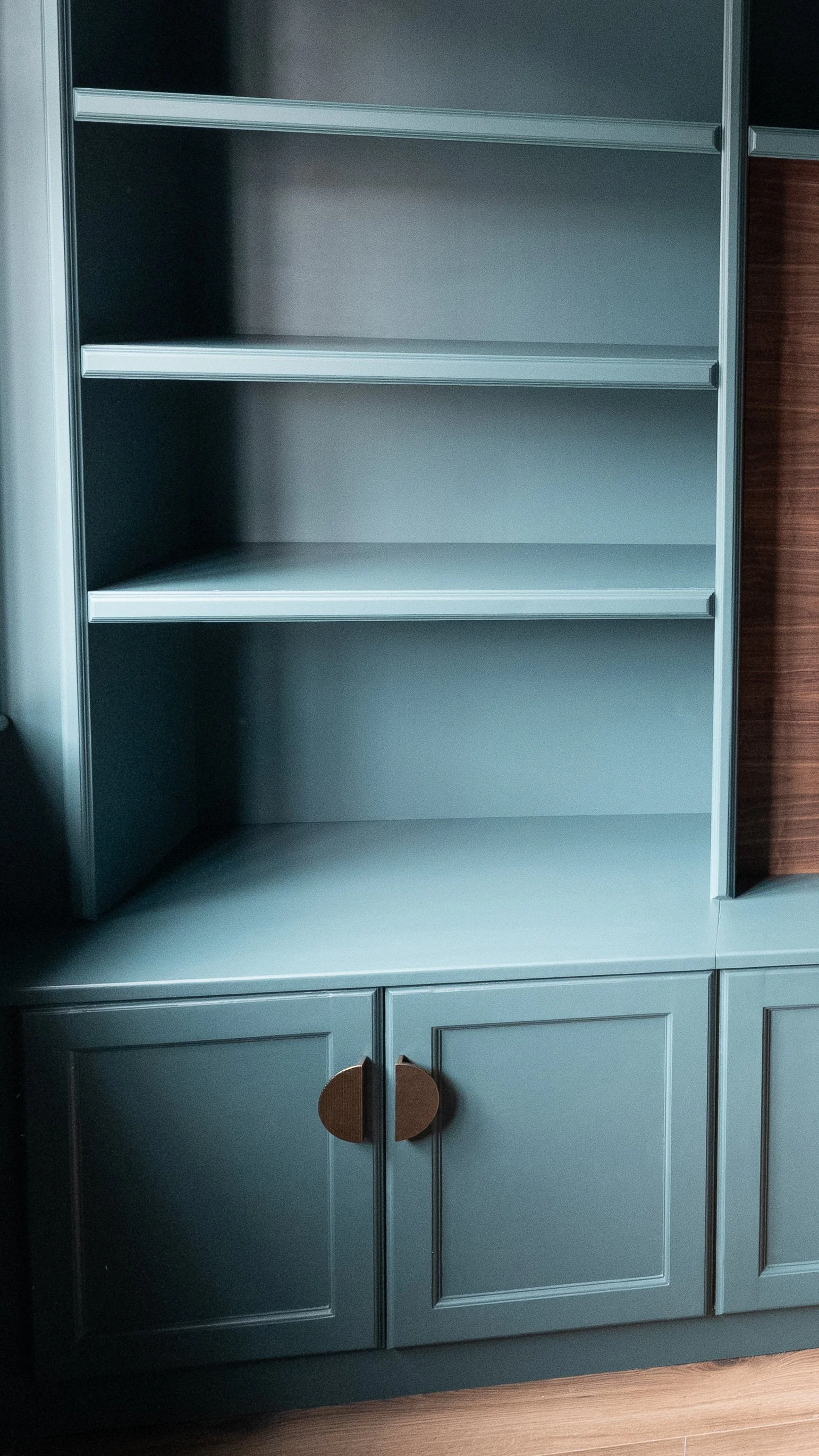 A green cabinet with open shelves on top and closed doors with wooden handles below, beside a wooden surface.