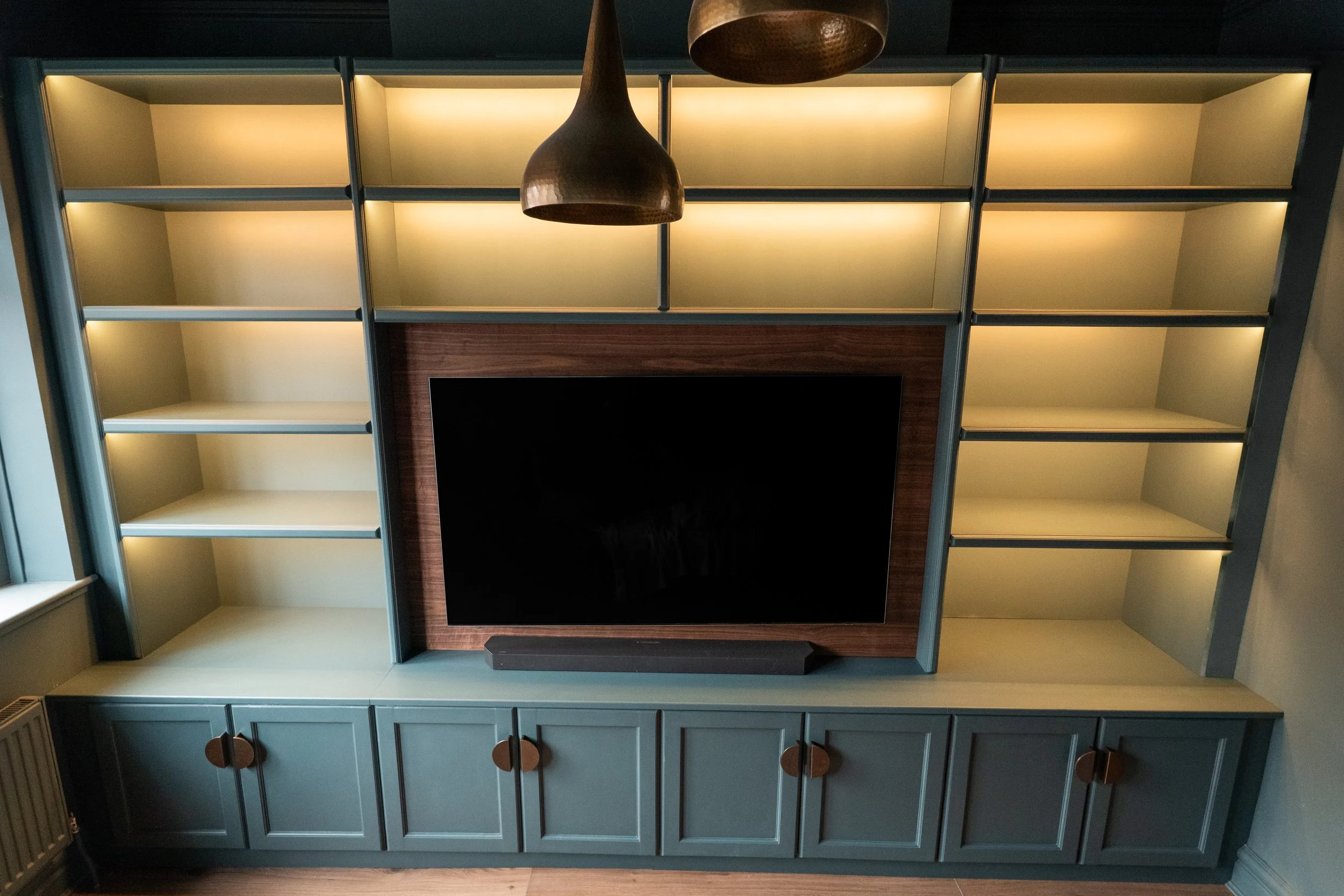 A wall unit with open shelving, a TV, and closed cabinets in a room. The wall unit is painted in blue with wooden knobs on the cabinets, and a wooden panel surrounds the TV.