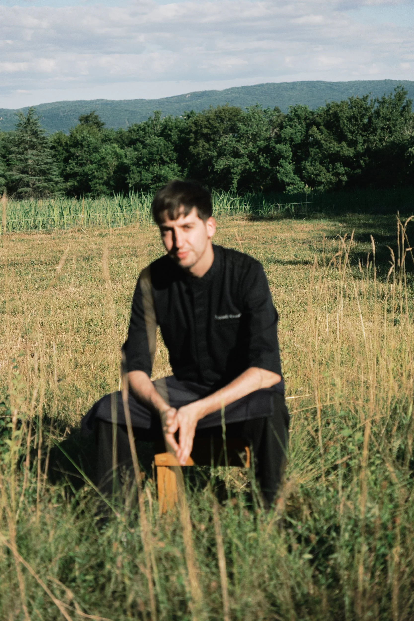 Le chef de l'Auberge de Marignat assis dans une prairie face aux montagnes du Jura, illustrant une cuisine inspirée par la nature et le terroir