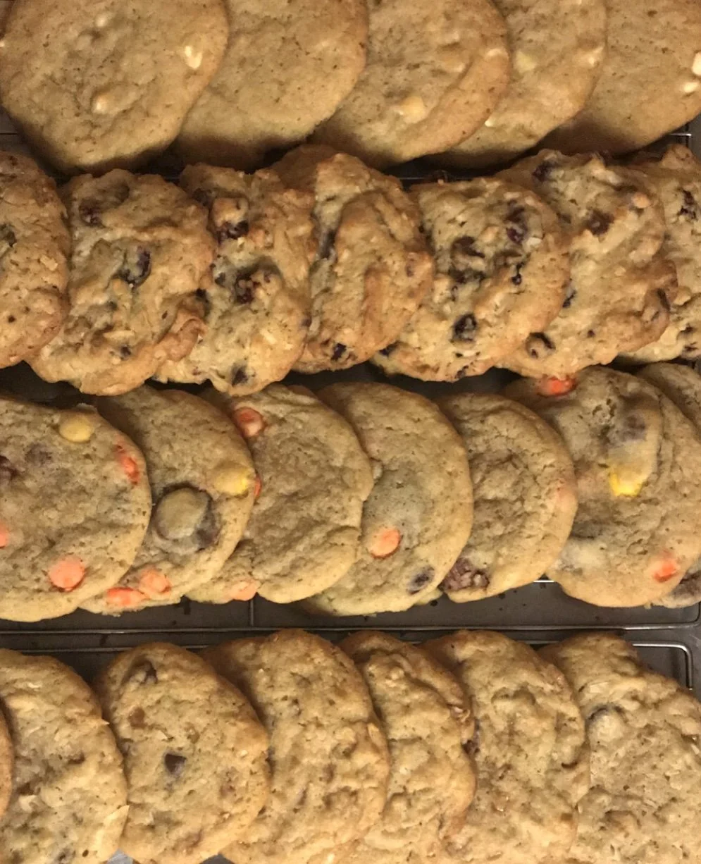 Assorted cookies on cooling racks, including chocolate chip, oatmeal raisin, and sugar cookies.