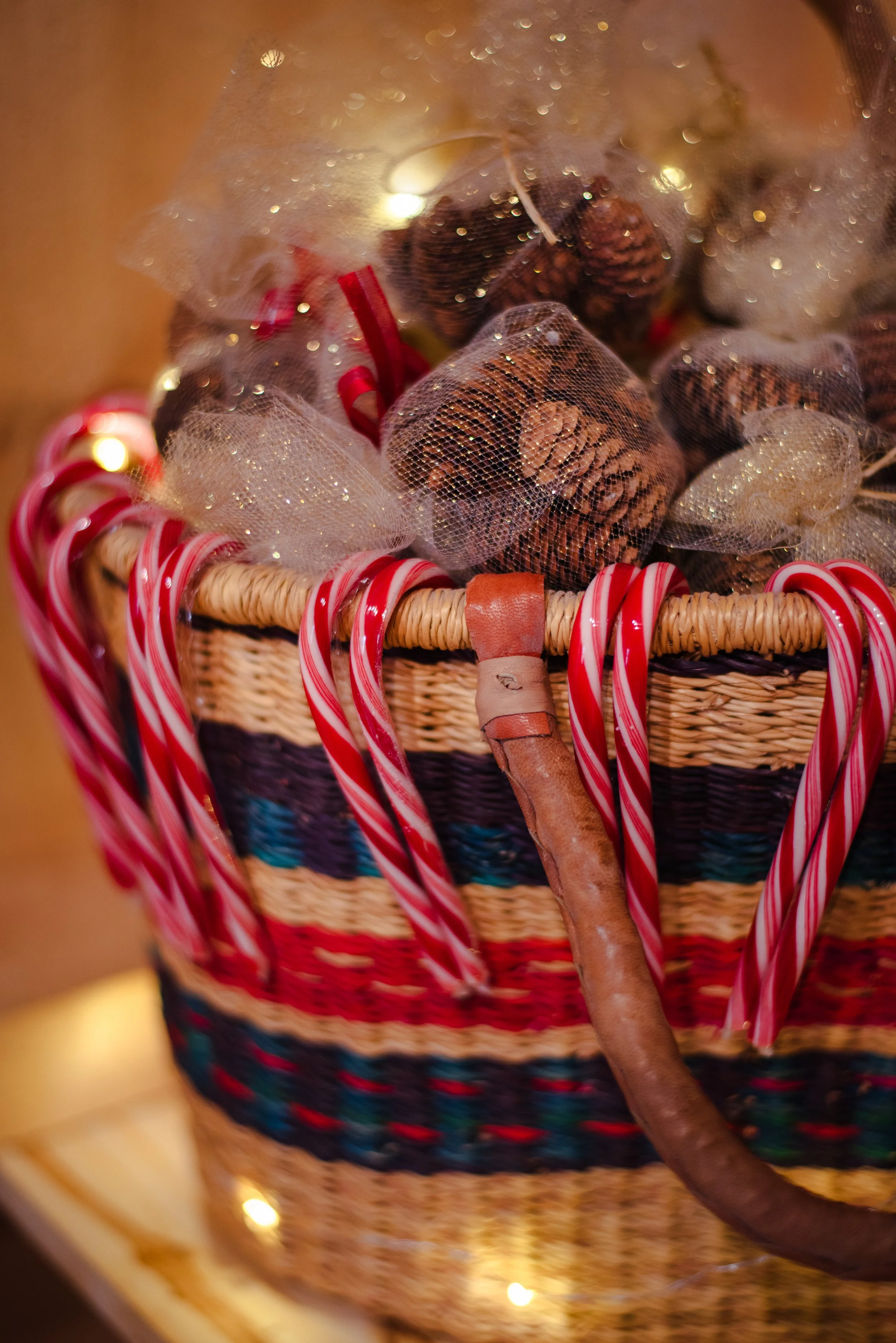 Close-up of a wicker basket filled with pinecones, candy canes, and decorative ribbons seen through a frosted glass surface.