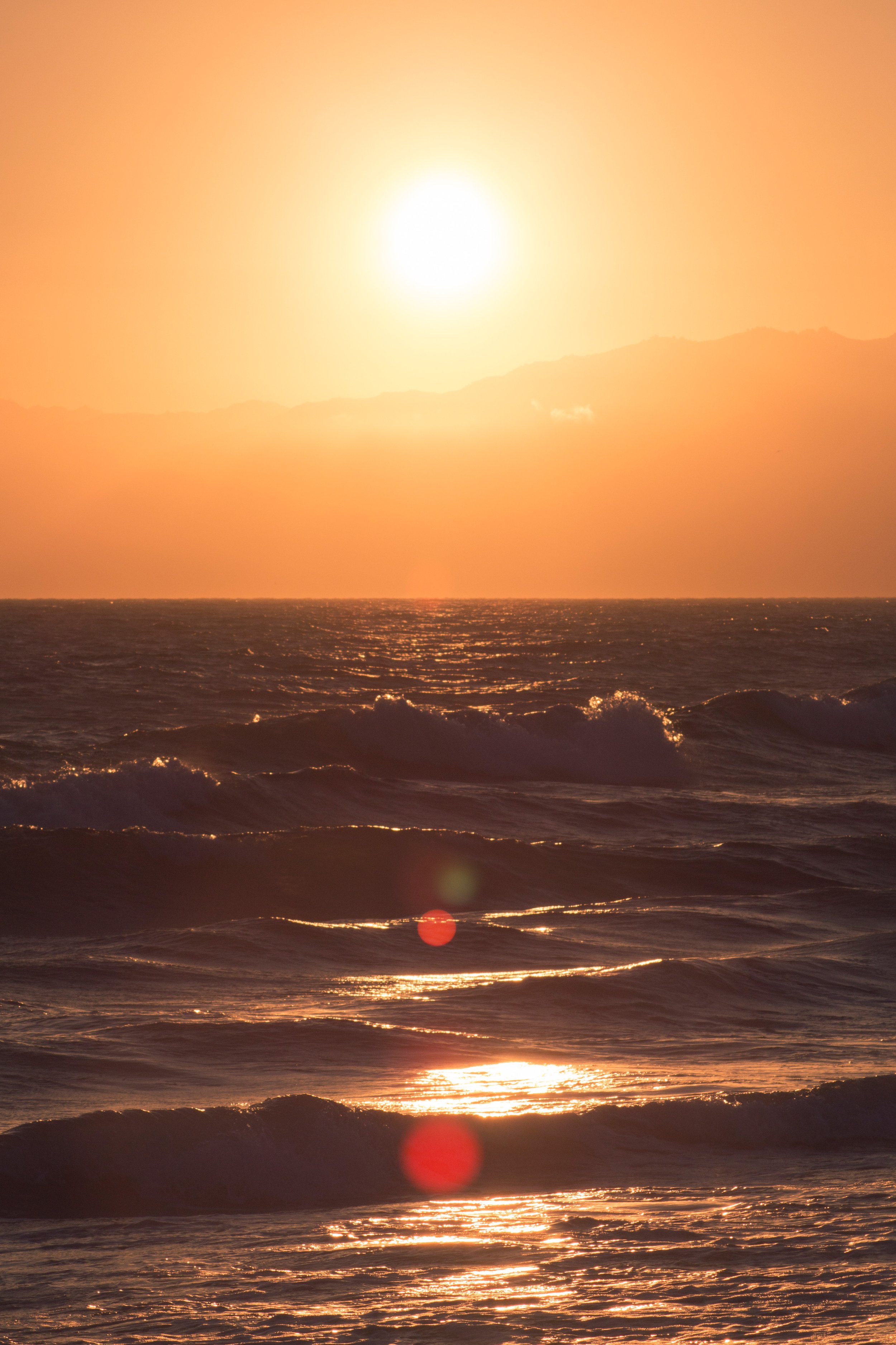 Solen falder ned over havet, og lyser den orangefarvede himmel op, mens bølger skvulper mod kysten.