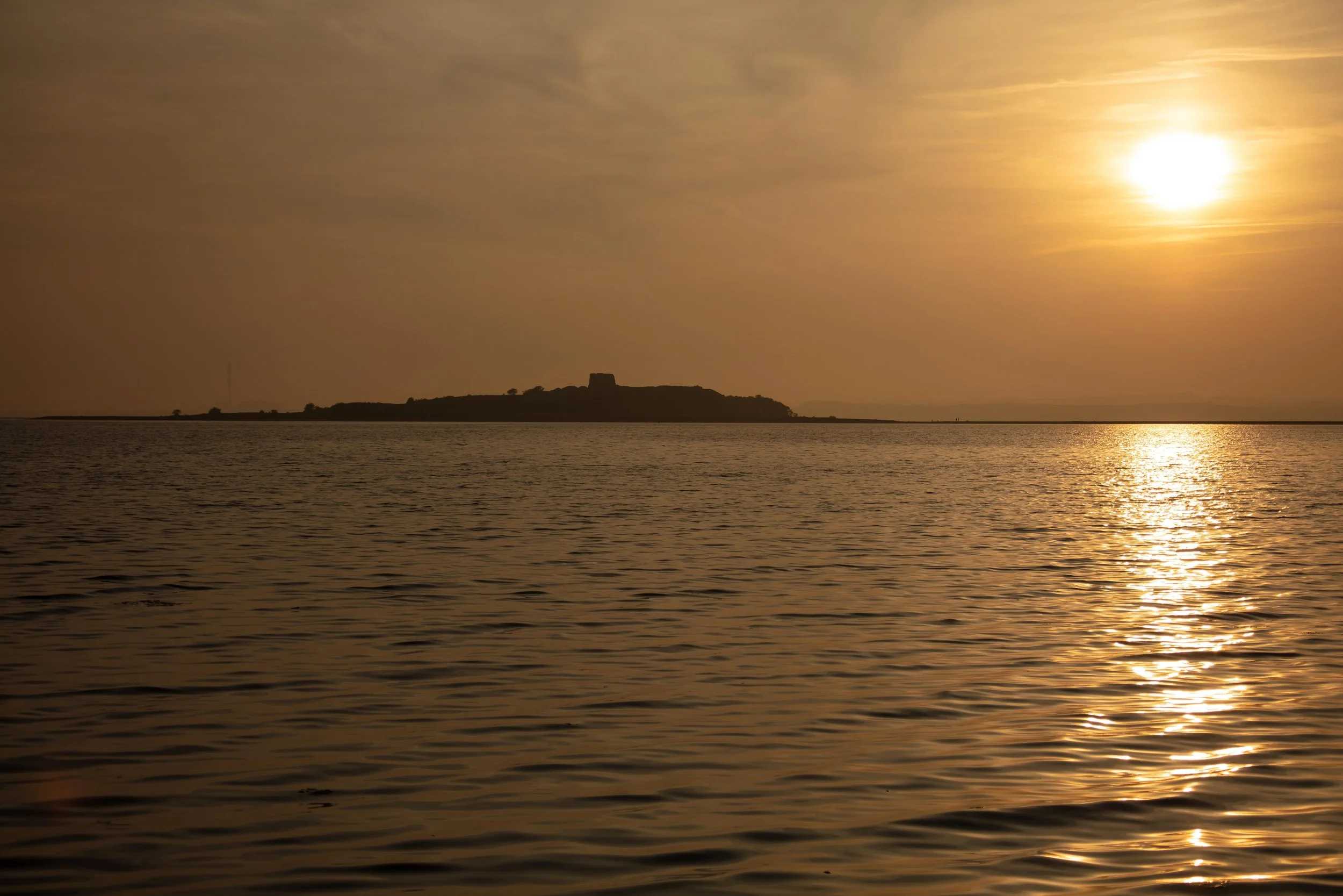En solnedgang over et vandlandskab med en ø i baggrunden og fredeligt vand.