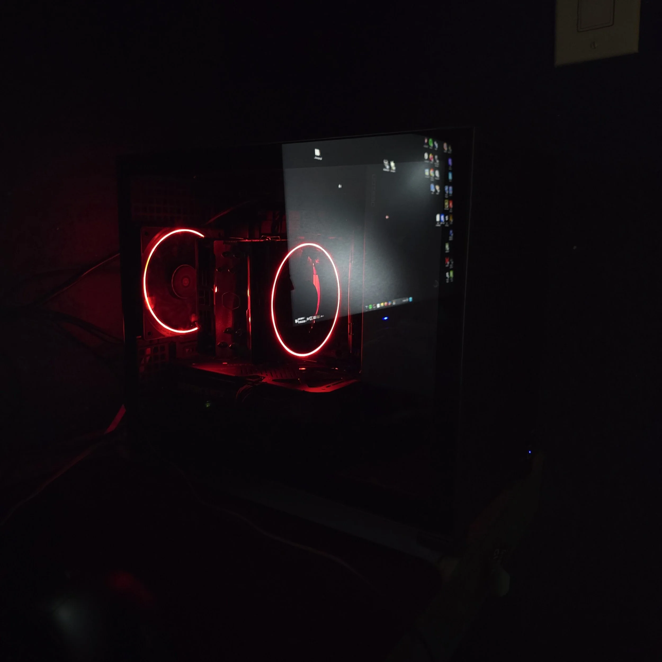 A dark room with a computer monitor displaying a desktop screen and red LED lights in the background.