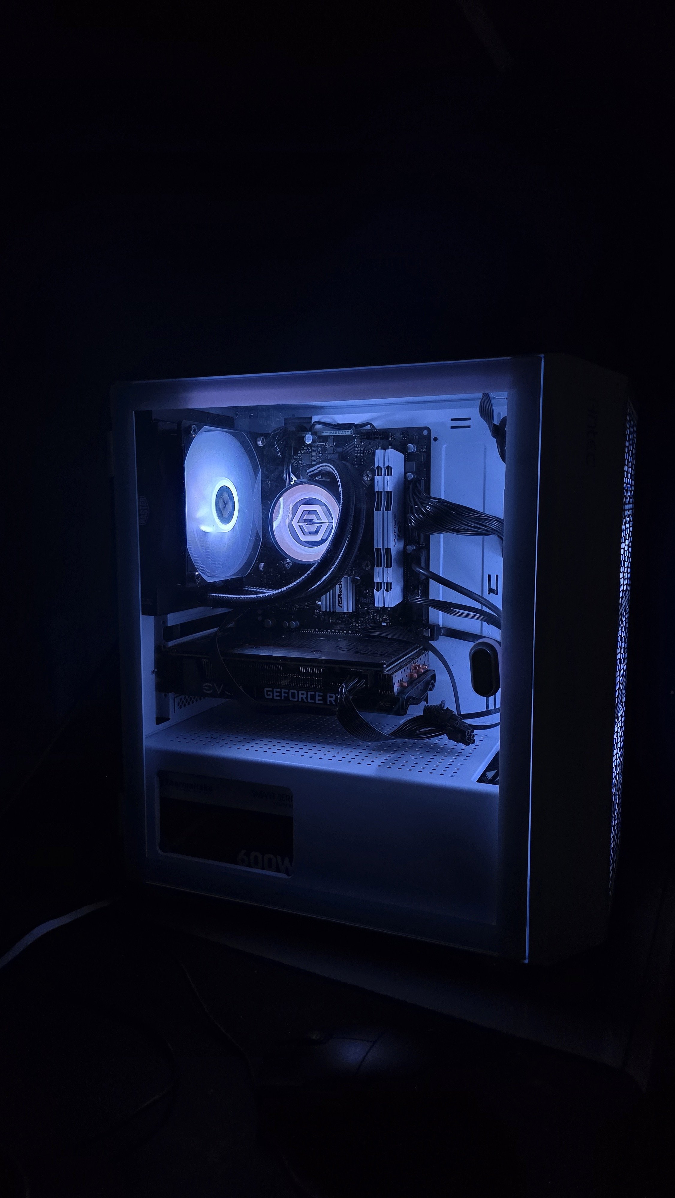 A gaming or computer desktop setup inside a white computer case with LED lighting, showing components like a graphics card, cooling system, and motherboard, in a dark room.