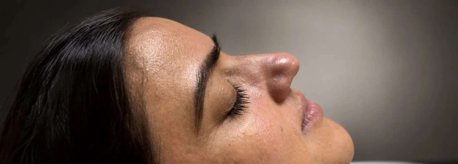 Close-up of a woman with her eyes closed, lying down, with smooth skin and long eyelashes.