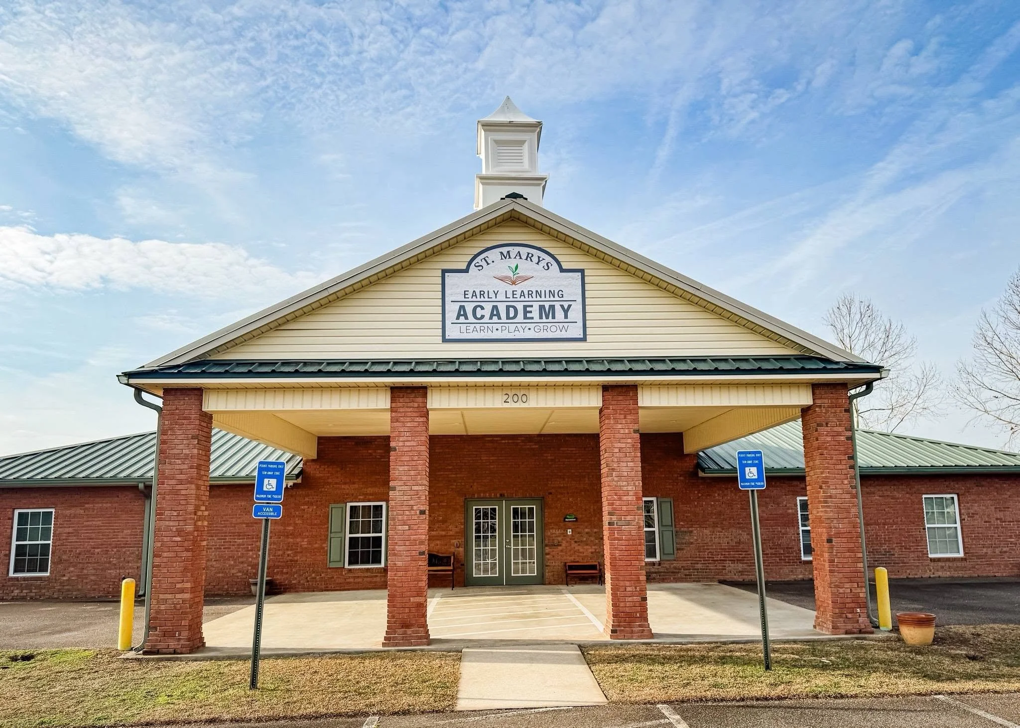 Front of St. Marys Early Learning Academy with a brick building, green door, and a sign overhead that reads 'Learn Play Grow'.
