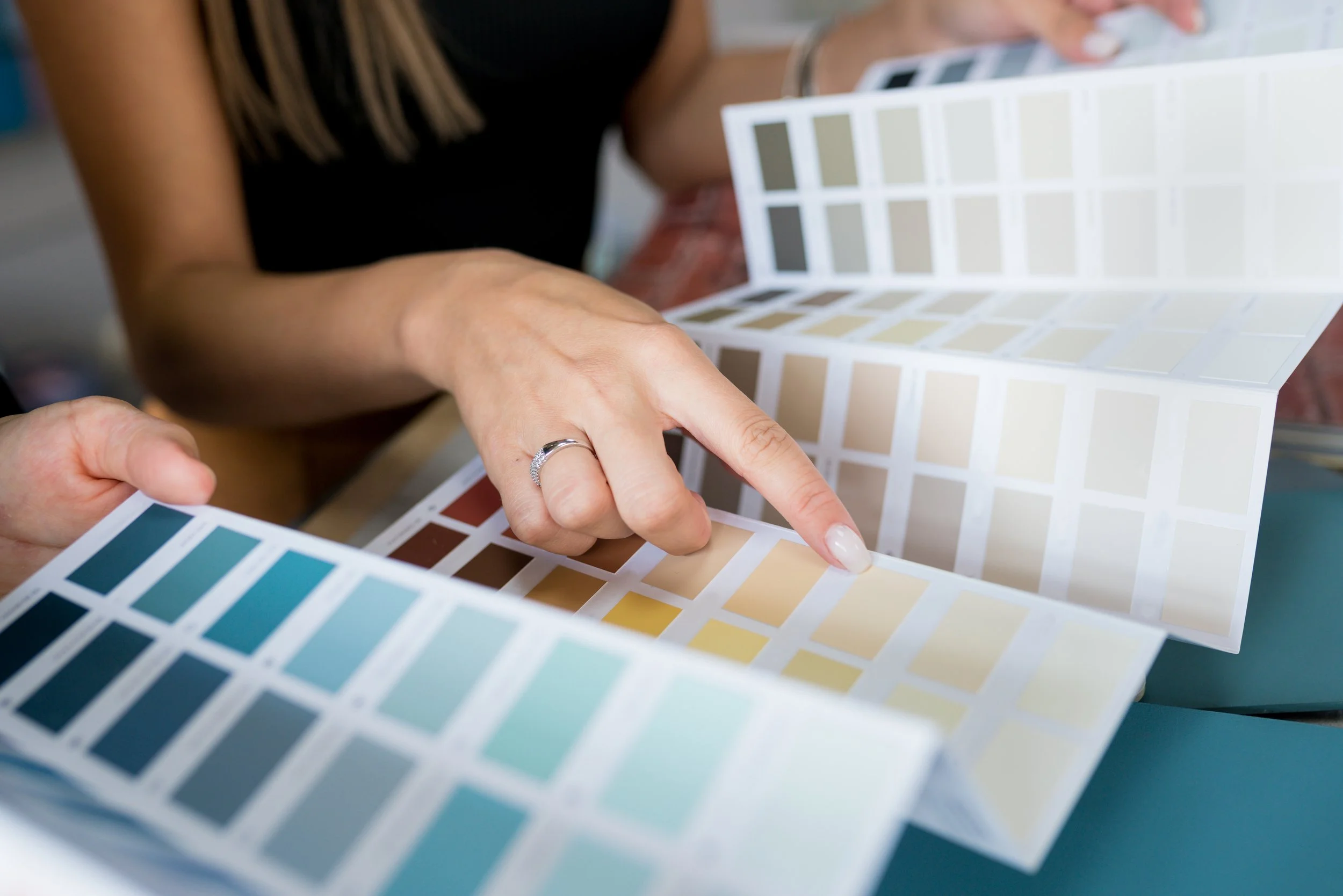 Person pointing at color swatches in a paint sample book.