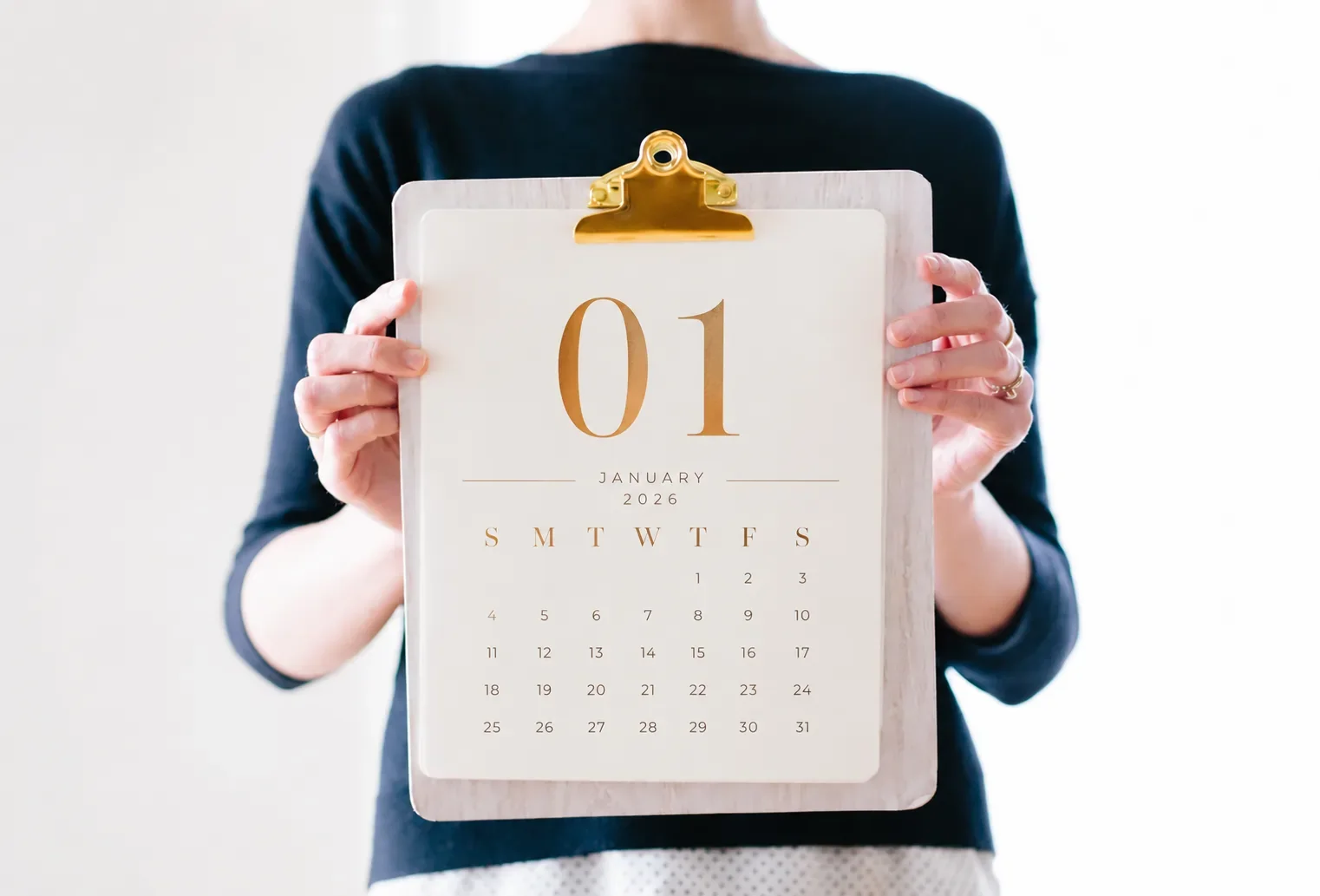 A woman is holding a calendar showing January 1, 2026, with the date displayed on a whiteboard held up in front of her.