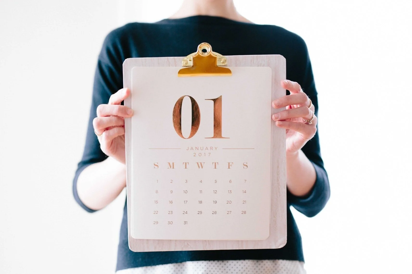 Person holding a desk calendar displaying January 1, 2017, with the person wearing a dark long-sleeve shirt.