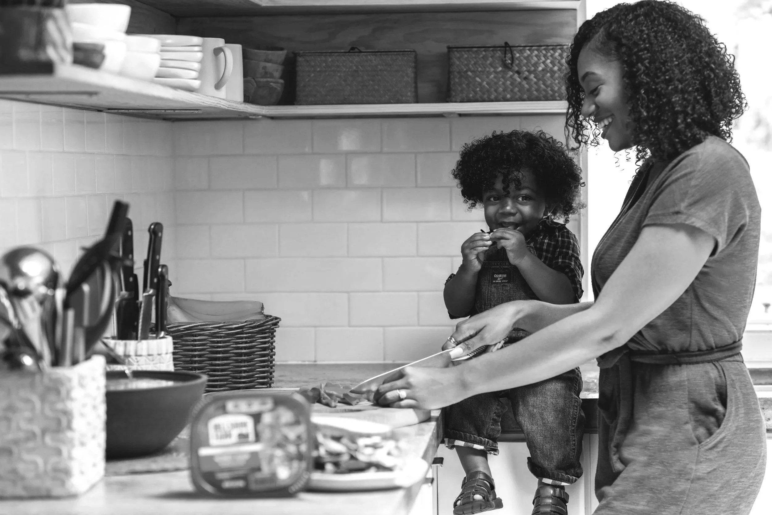 A woman and a young girl in the kitchen, smiling and preparing food together at the counter.