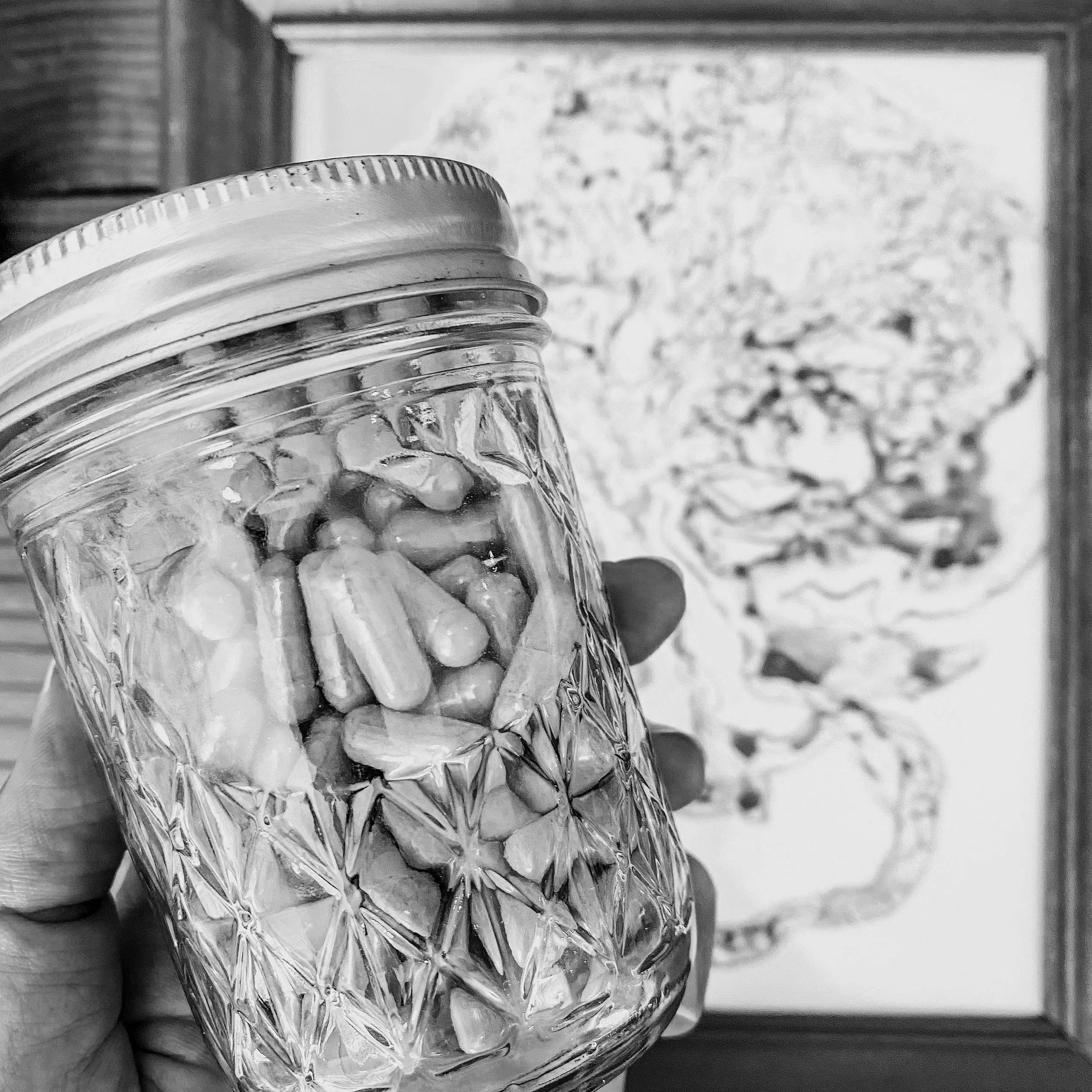 Close-up of a glass jar with a metal lid, held in hand in front of a window with a blurry outdoor scene.