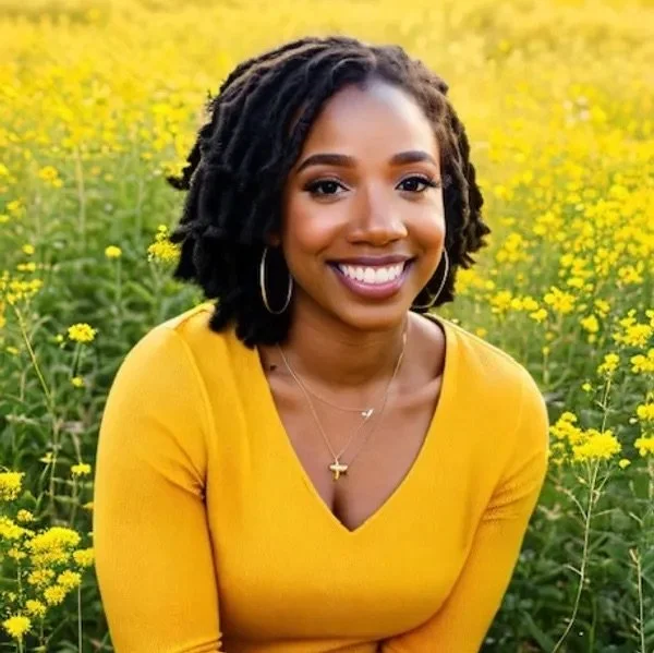 A smiling woman with dark curly hair wearing a yellow top and gold jewelry in a yellow flower field.