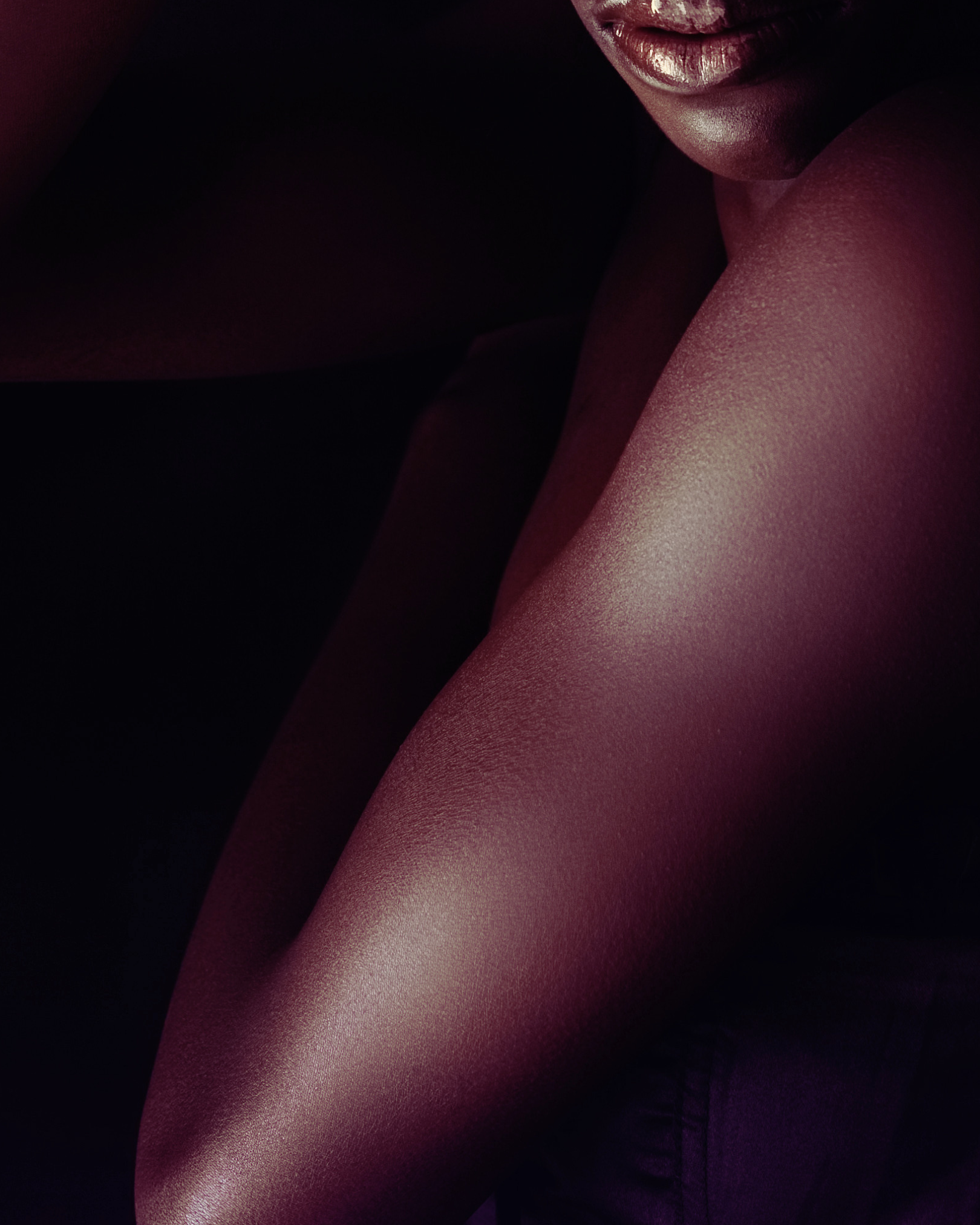 Close-up of a woman's lips and shoulder, with smooth skin and a dark background.