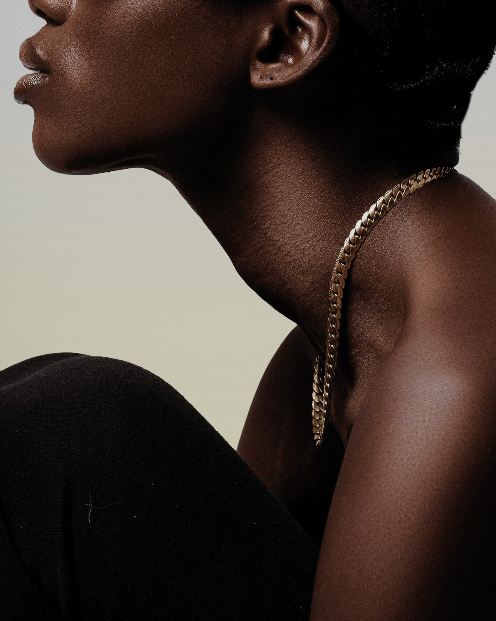 Close-up side profile of a woman with dark skin wearing a gold chain necklace and black clothing.