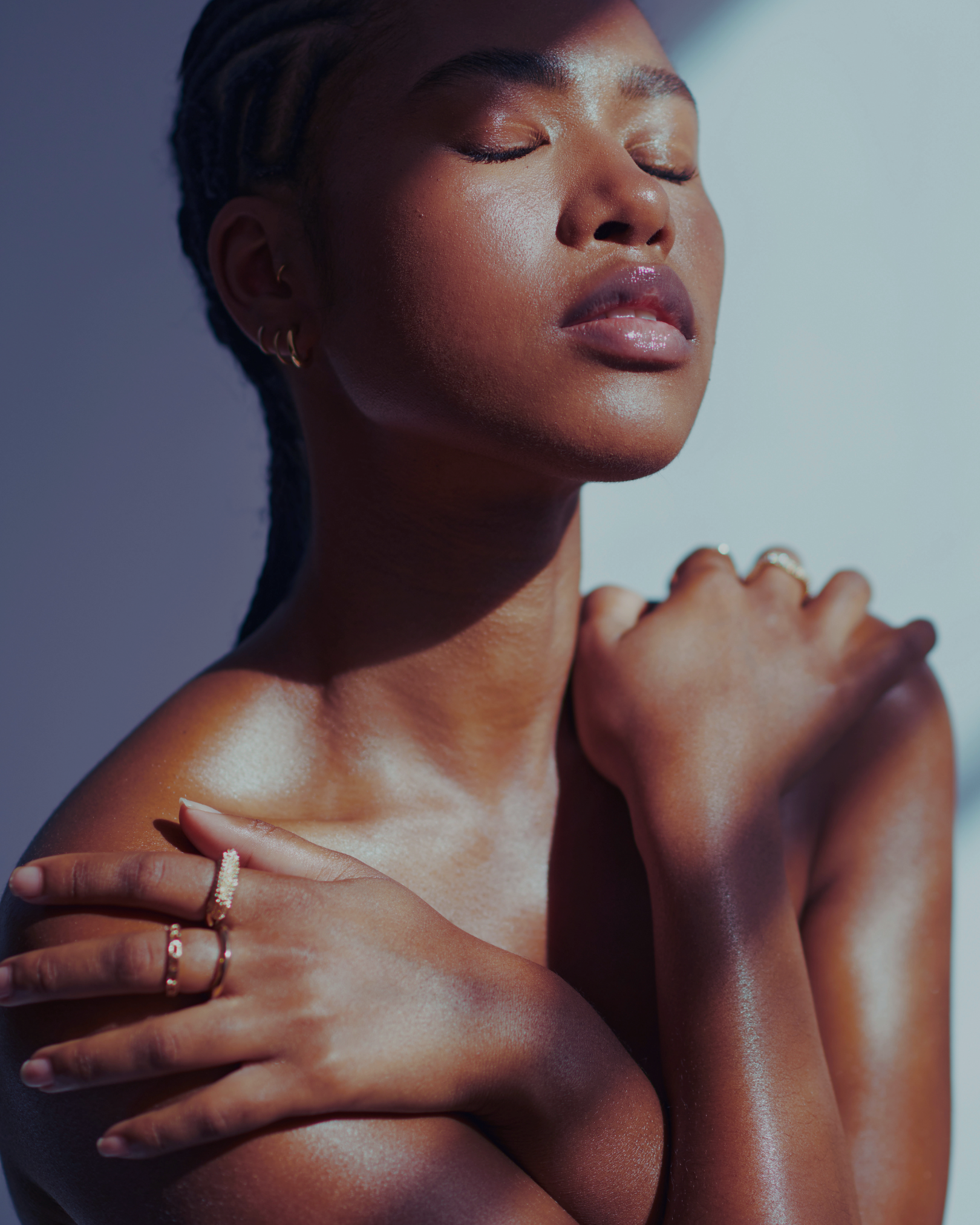 A portrait of a woman with her eyes closed, her hand on her shoulder, wearing multiple rings, with a focus on her face and jewelry.