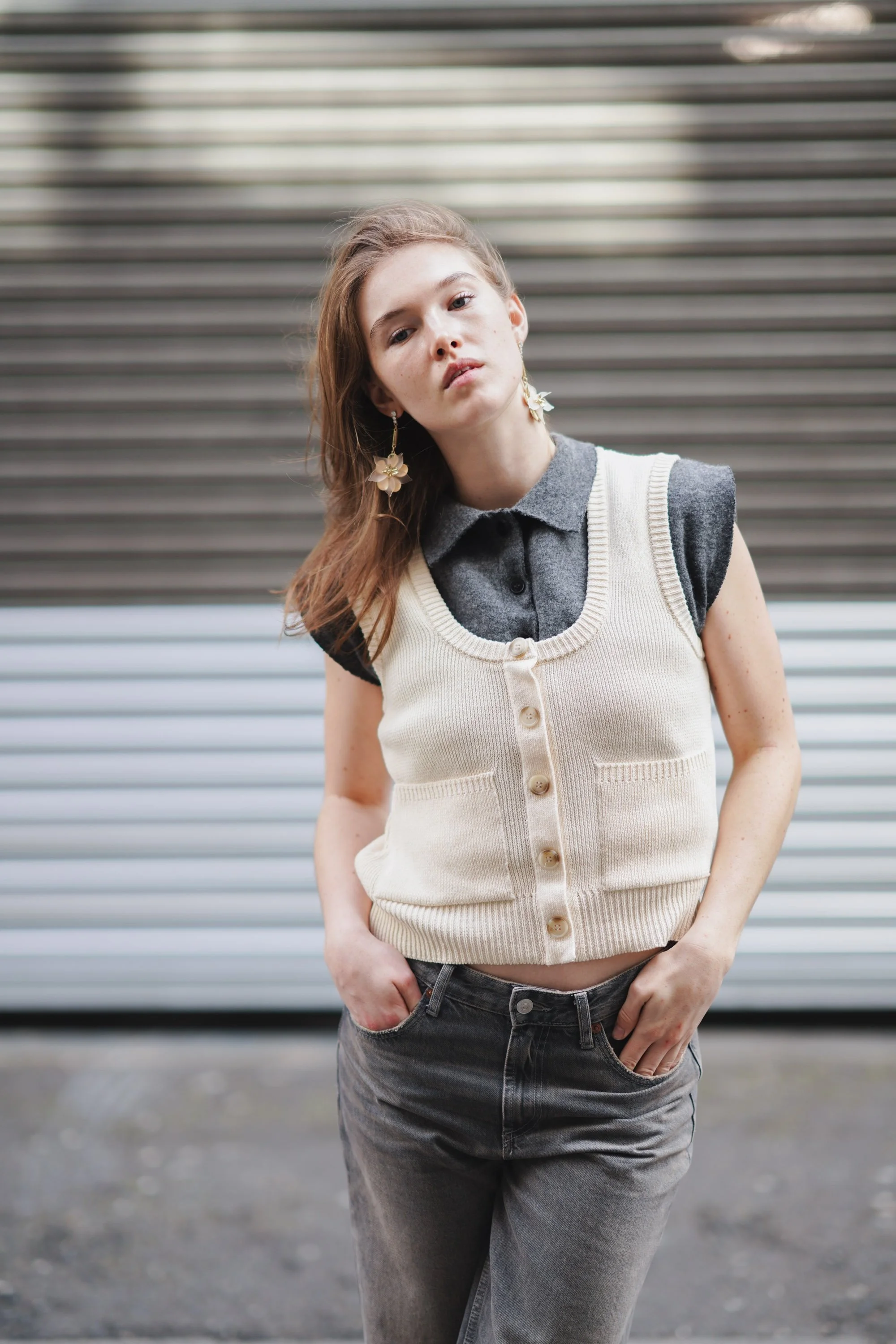 A young woman with long brown hair and earrings posing in front of a metallic, horizontally-striped background.