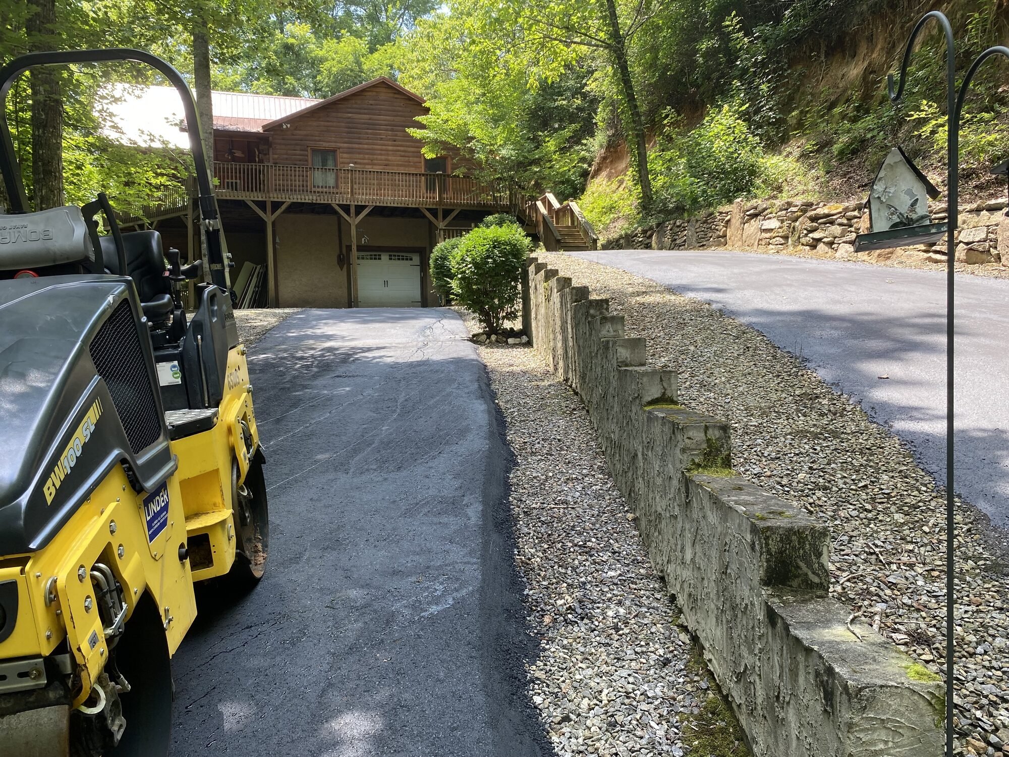Asphalt roller compacting a new driveway beside a stone wall at a mountain home in Whittier, Jackson County NC — Black Bear Paving