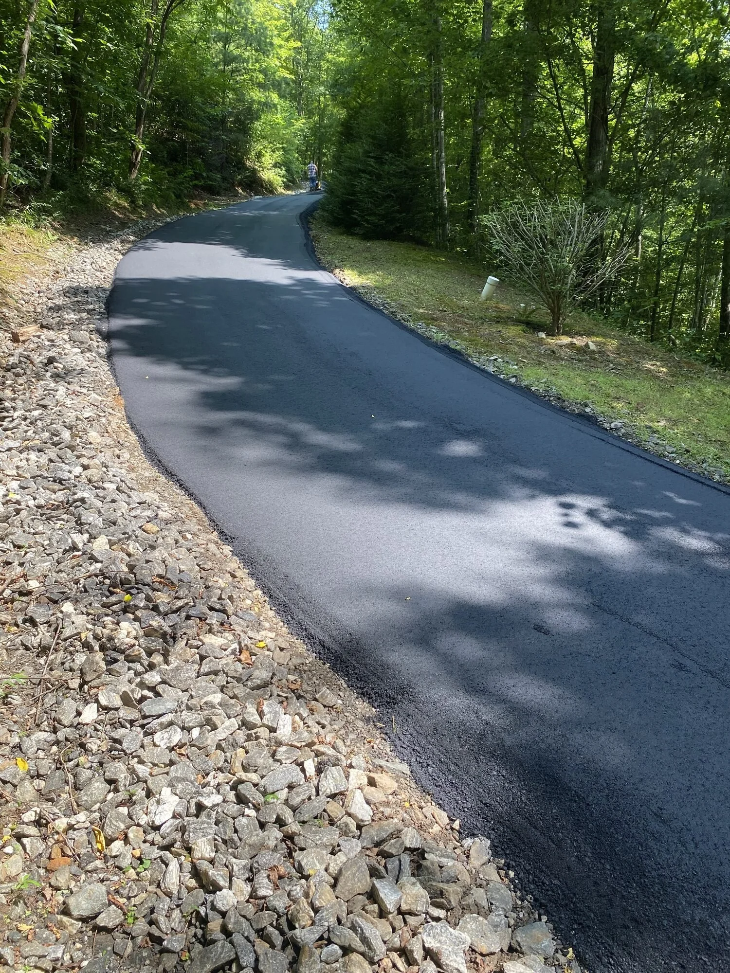 Freshly laid asphalt driveway with a new gravel shoulder curving through the woods in Jackson County, NC — Black Bear Paving