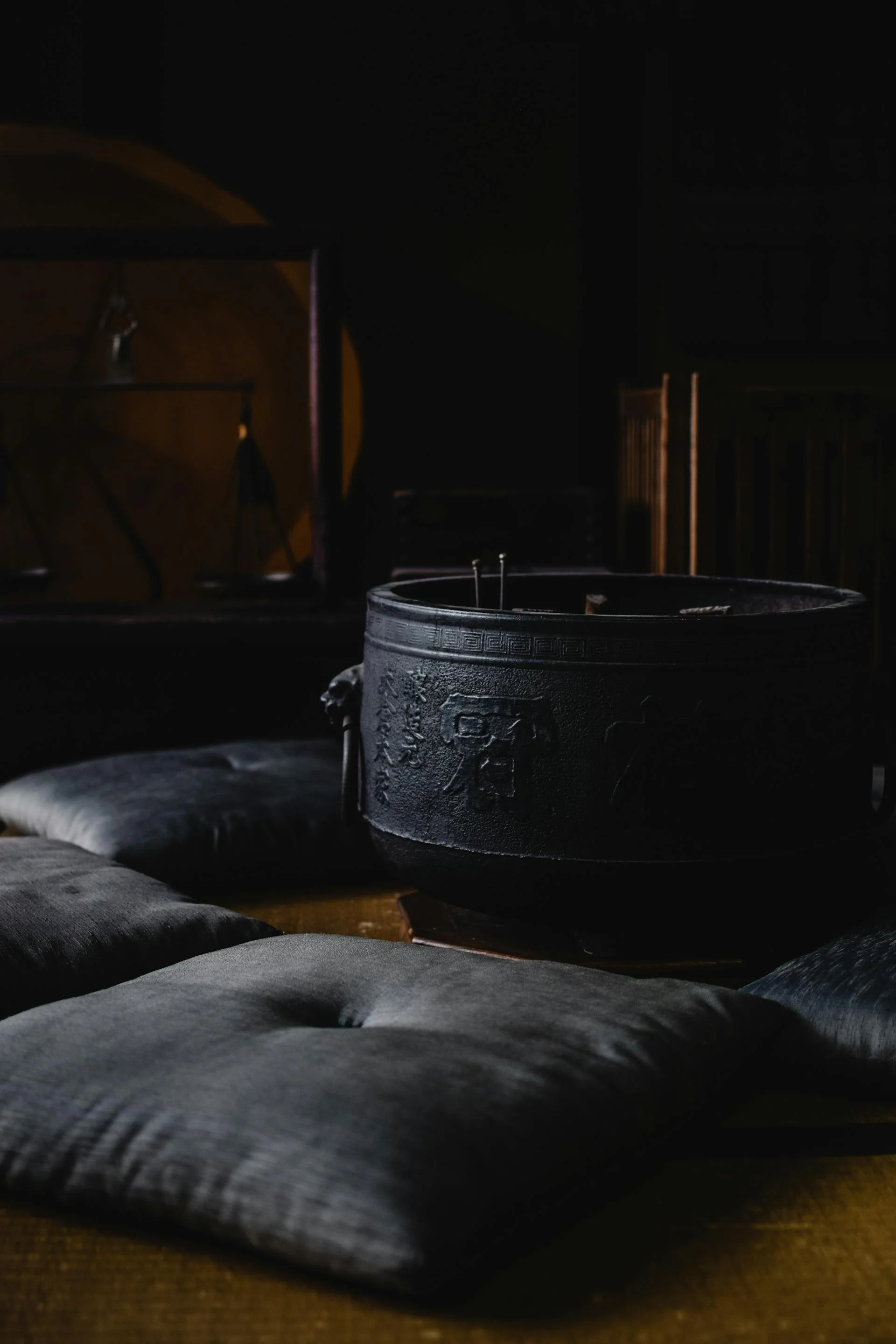 Wedding Website Design, Digital Wedding Stationery, Web Design and Branding for Wedding Professionals | Avelã White. Traditional Japanese iron tea pot on a wooden floor surrounded by dark brown cushions in a dimly lit room.