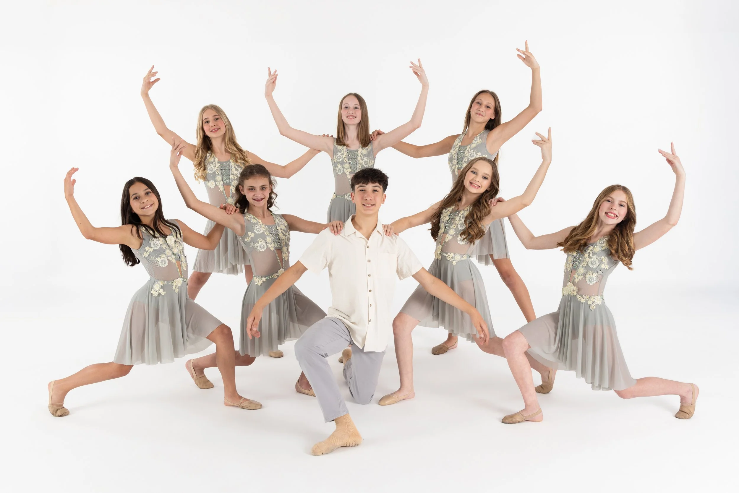 A group of eight young ballet dancers and one male instructor posing in dance positions against a white background.