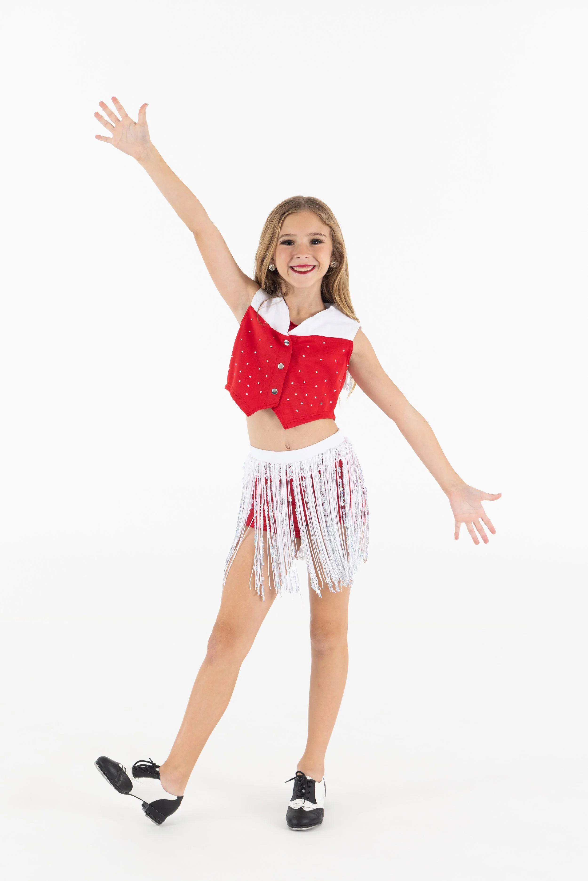 Young girl dancing or performing figure skating moves on ice, wearing a red and white costume, black ice skates, and smiling.