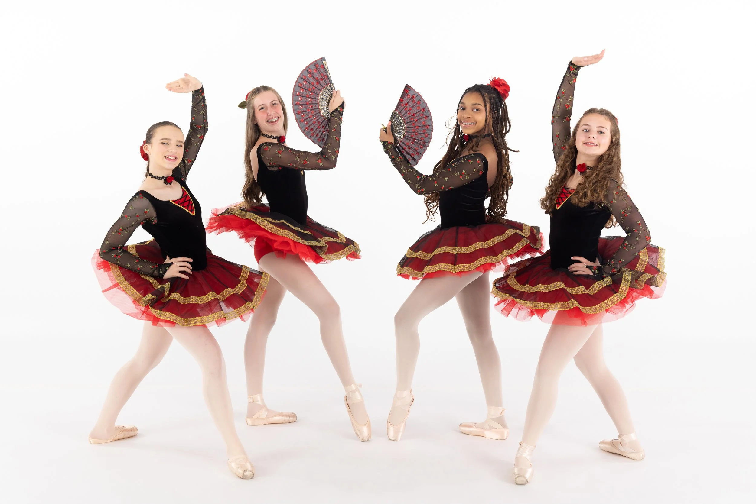 Four young girls dressed as ballerinas in black and red costumes, holding fans, posing with one arm raised, on a white background.