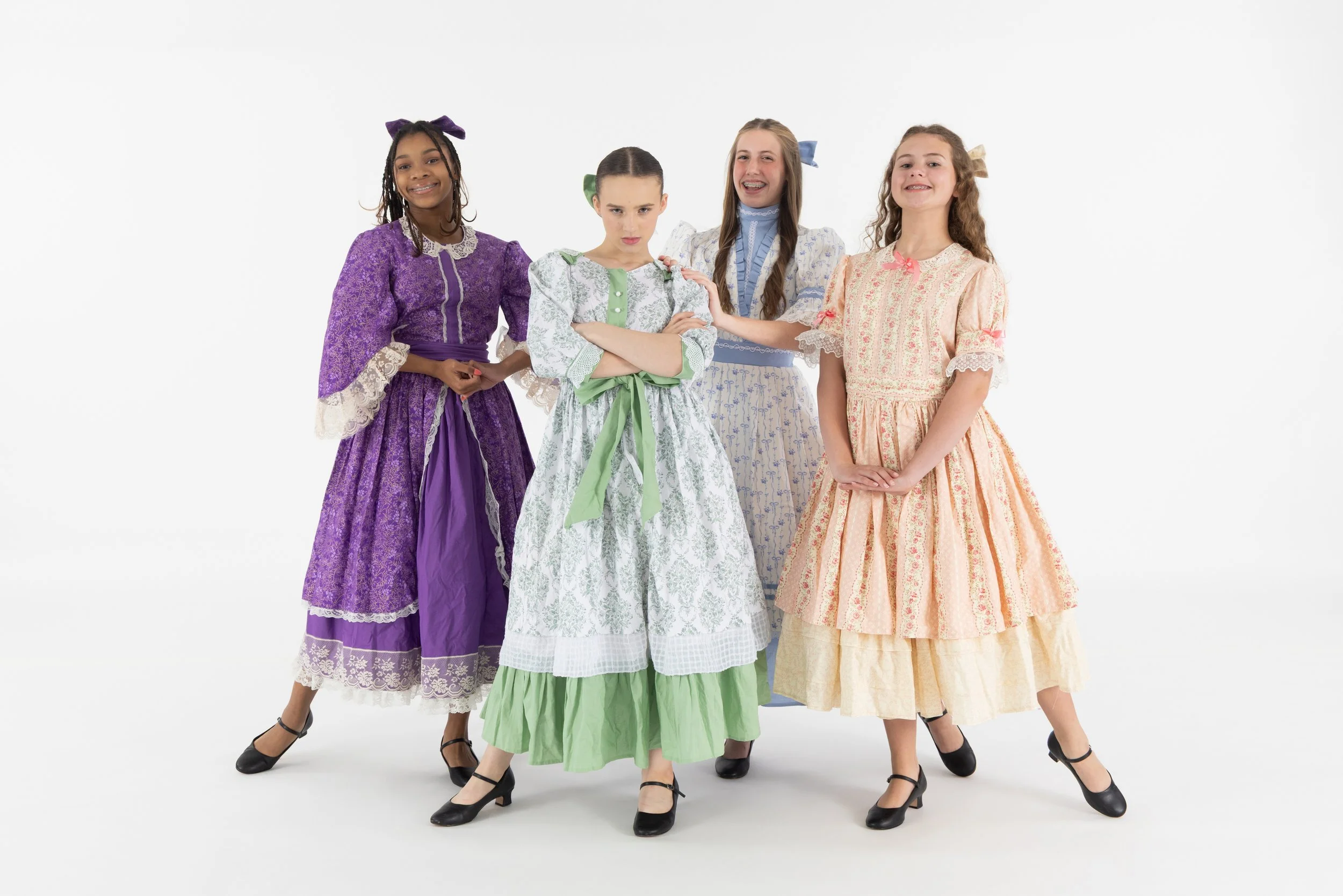 Four girls dressed in vintage-style dresses standing together against a white background.