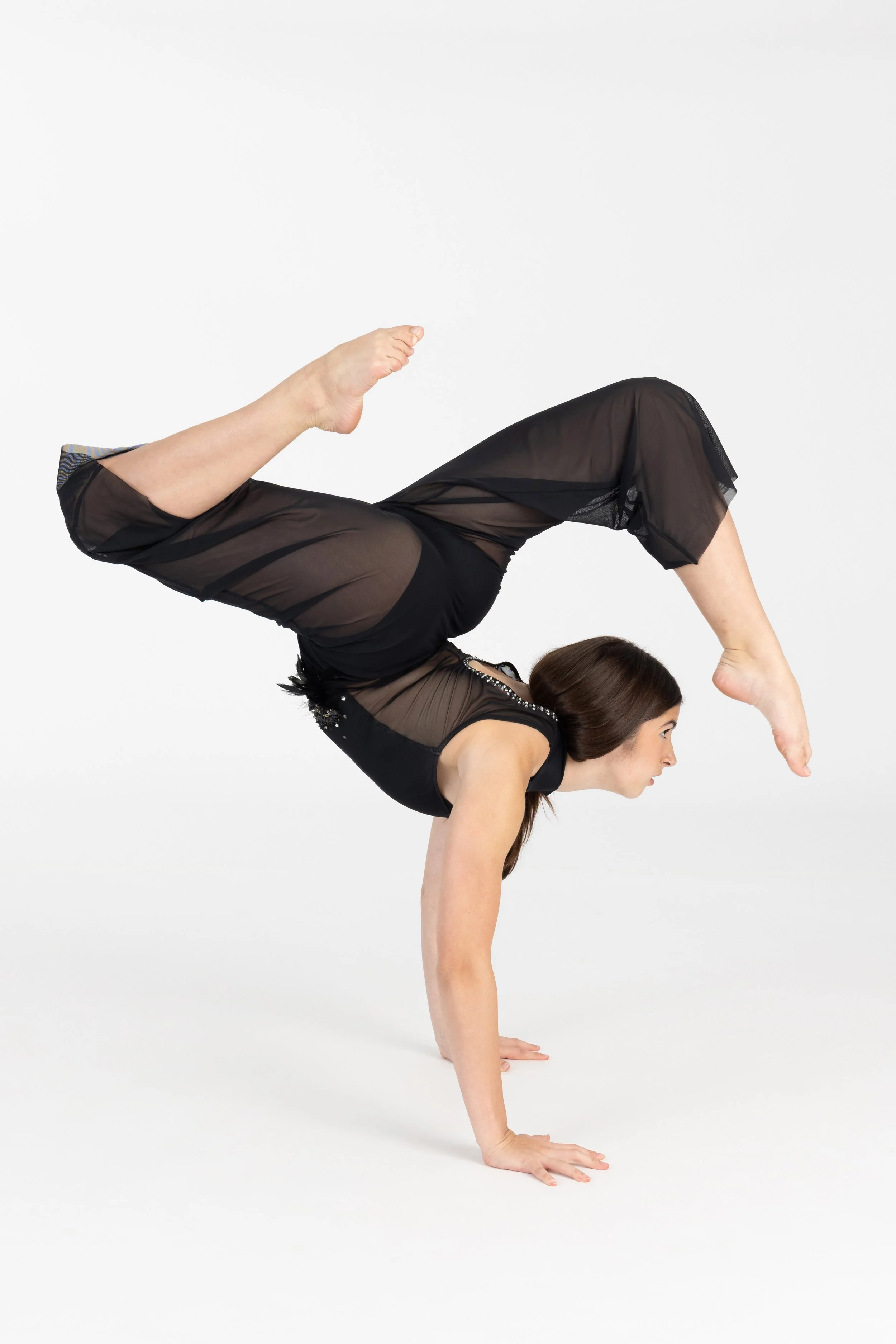 A woman performing a handstand in a yoga pose, balancing on her hands with her legs bent and one foot touching her head, on a white background.