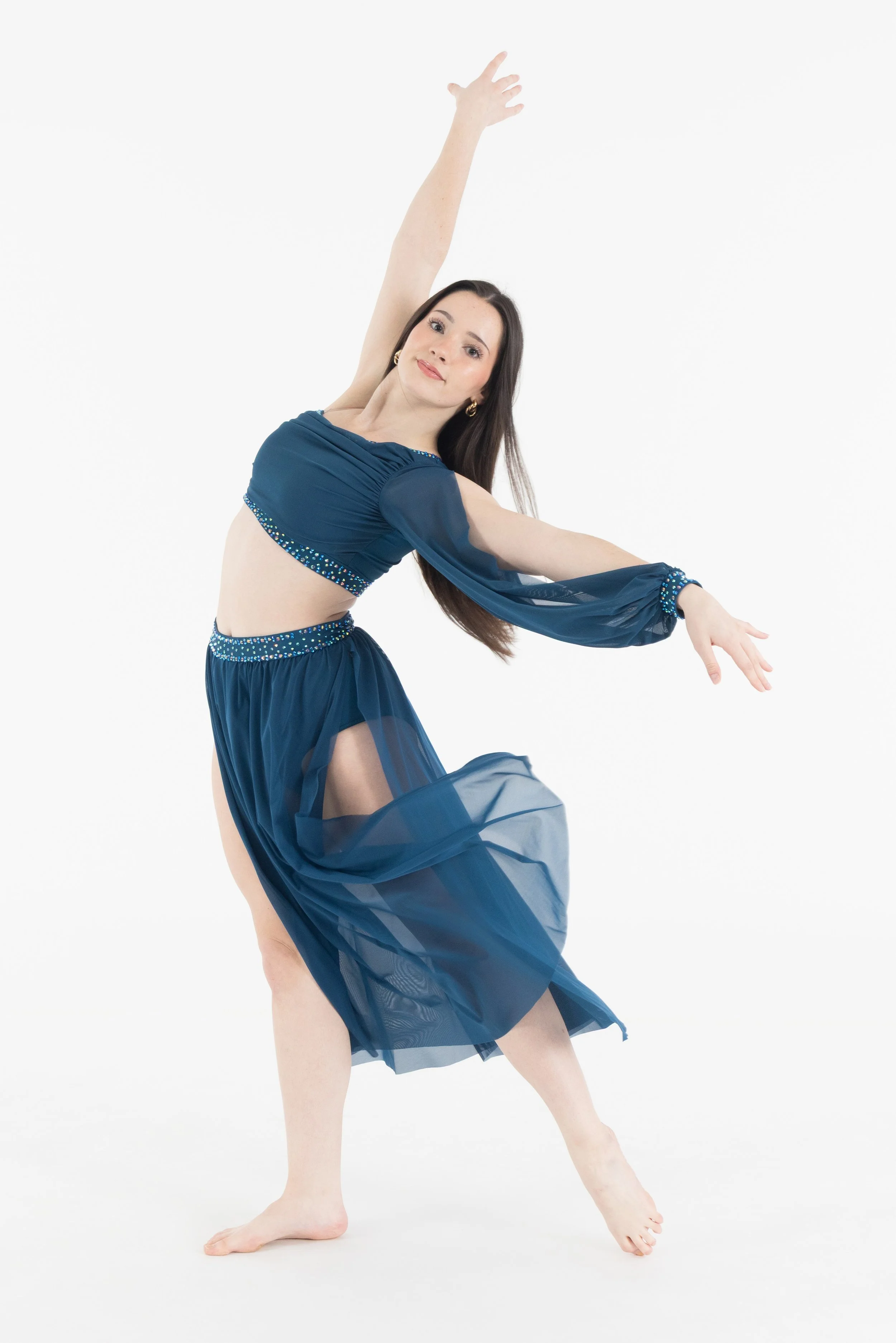 A woman in a blue dance costume with sheer fabric and rhinestone details performs a dance pose against a plain white background.