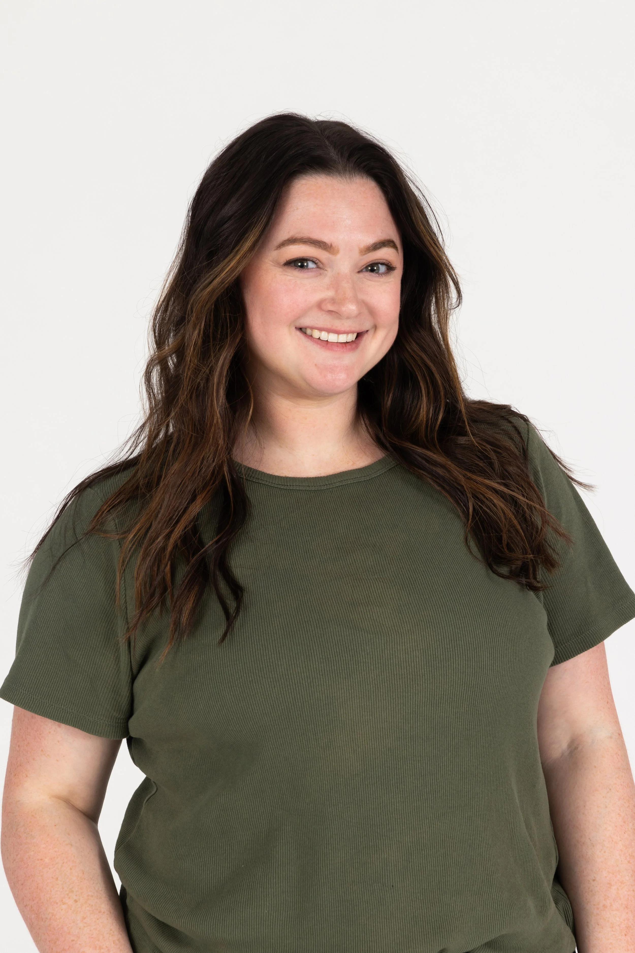 Close-up of a woman with long brown hair, smiling, wearing a green t-shirt, against a plain white background.