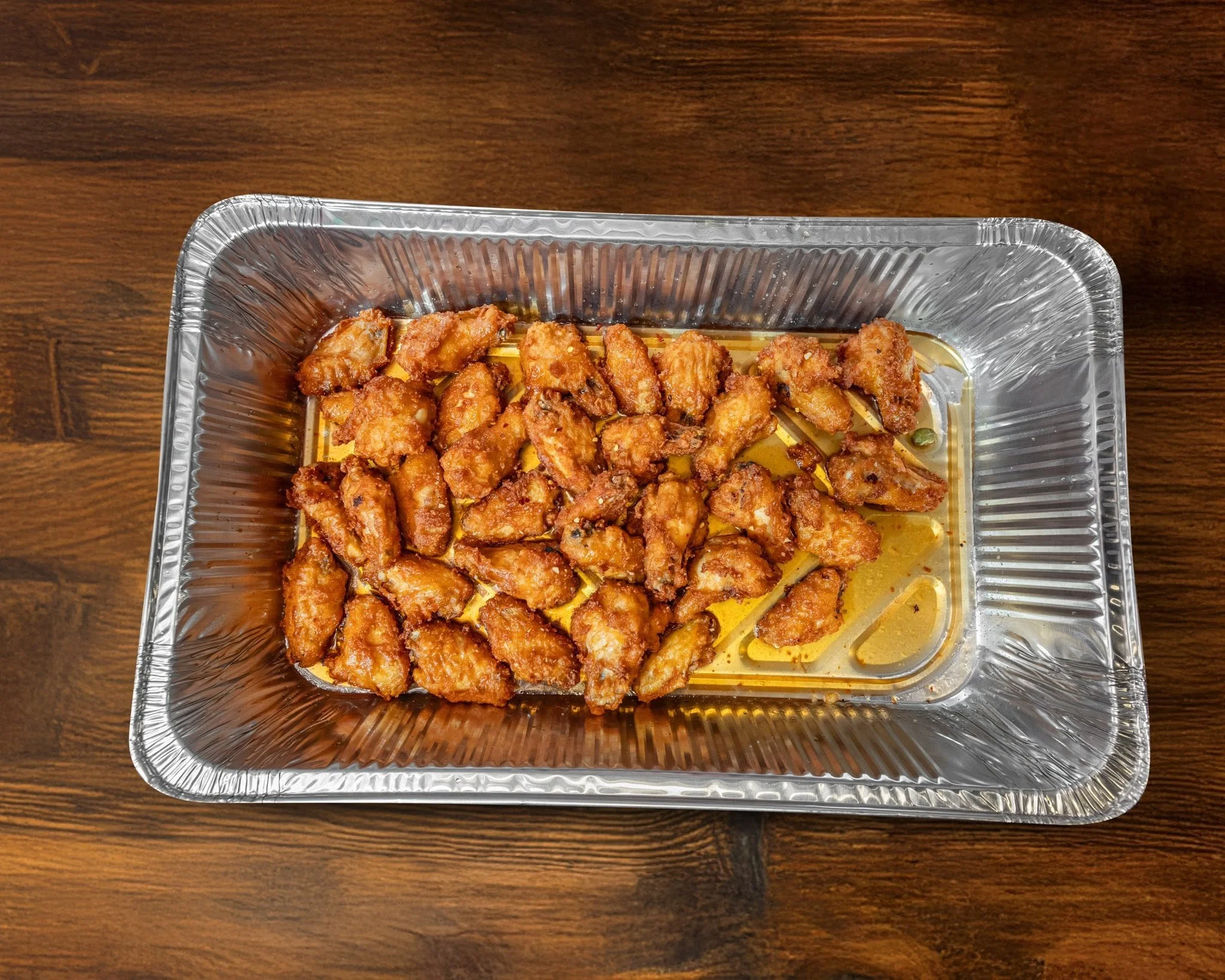 Fried chicken pieces in a foil tray on a wooden surface
