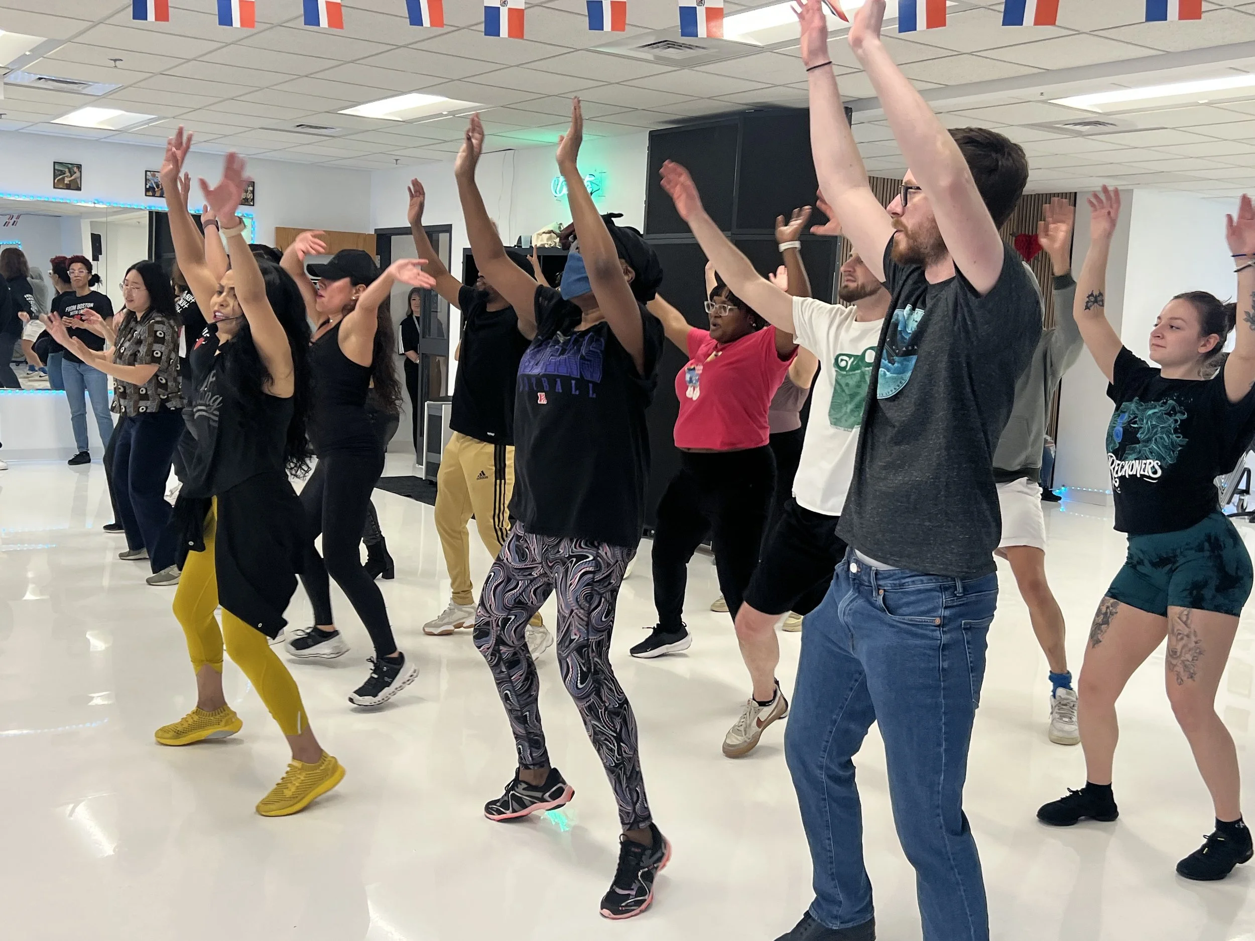 Group of diverse people participating in a dance or exercise class indoors, with American flags hanging above.